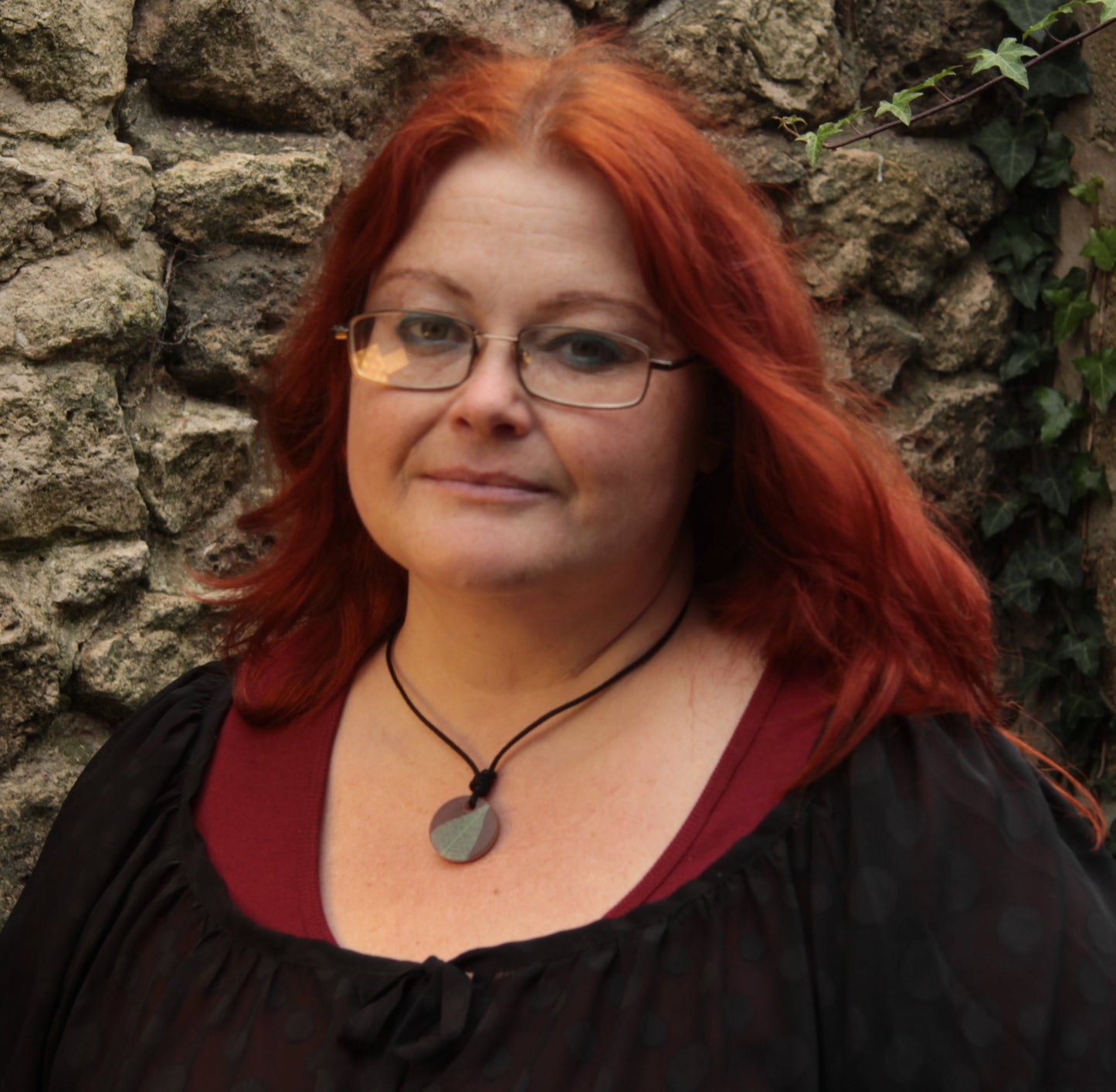 Red haired woman wearing a warm brown round pendant with pale green leaf skeleton design