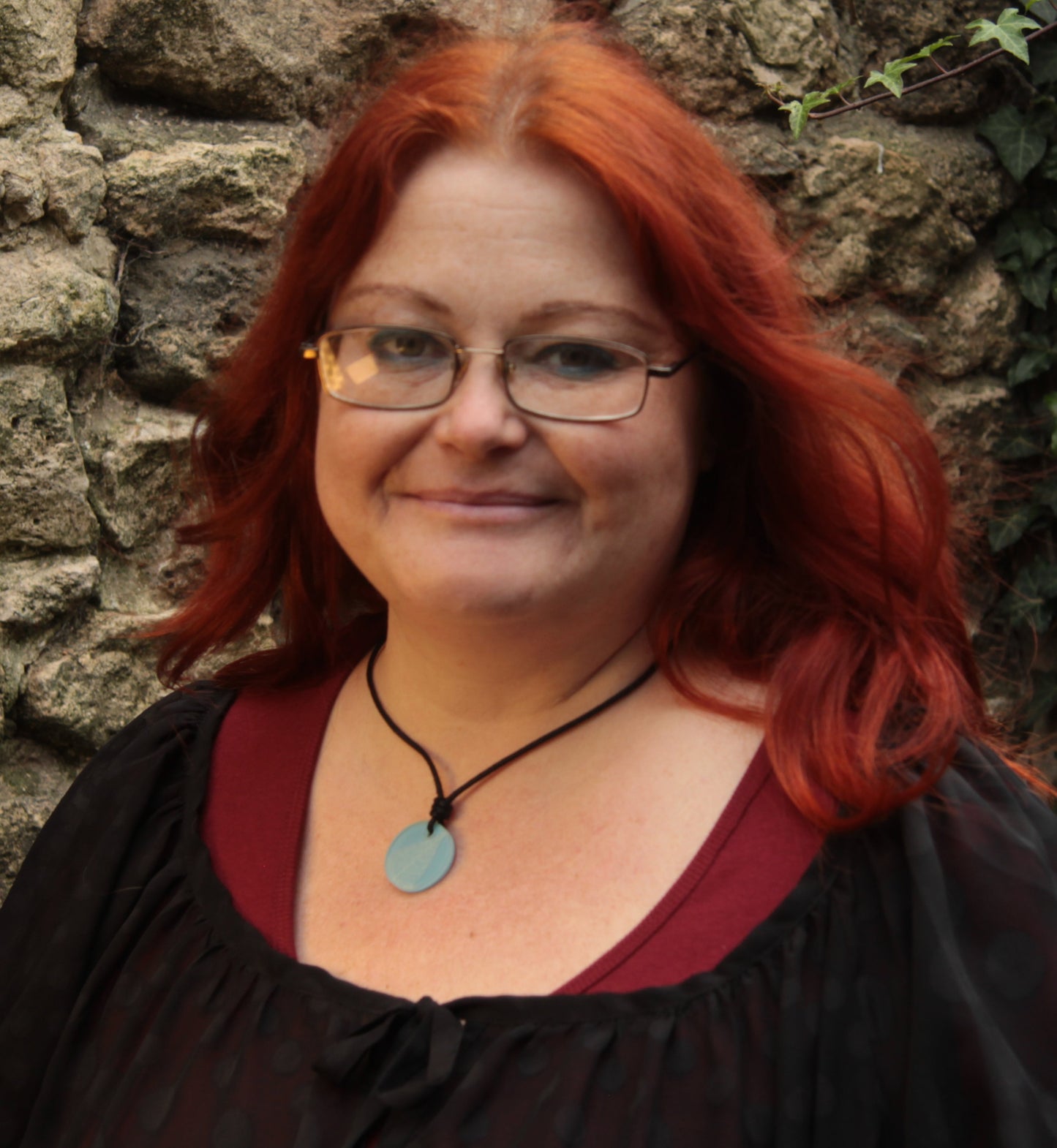 Red haired woman wearing a light blue round pendant with white leaf skeleton design