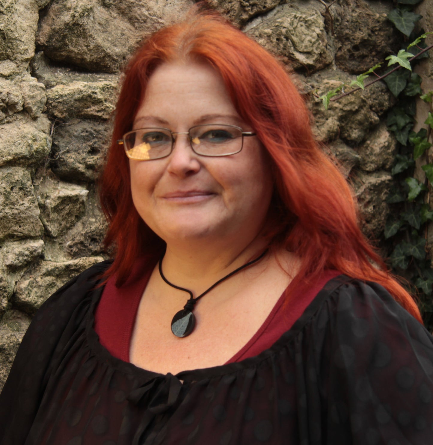Red haired woman wearing a black round pendant with white leaf skeleton design
