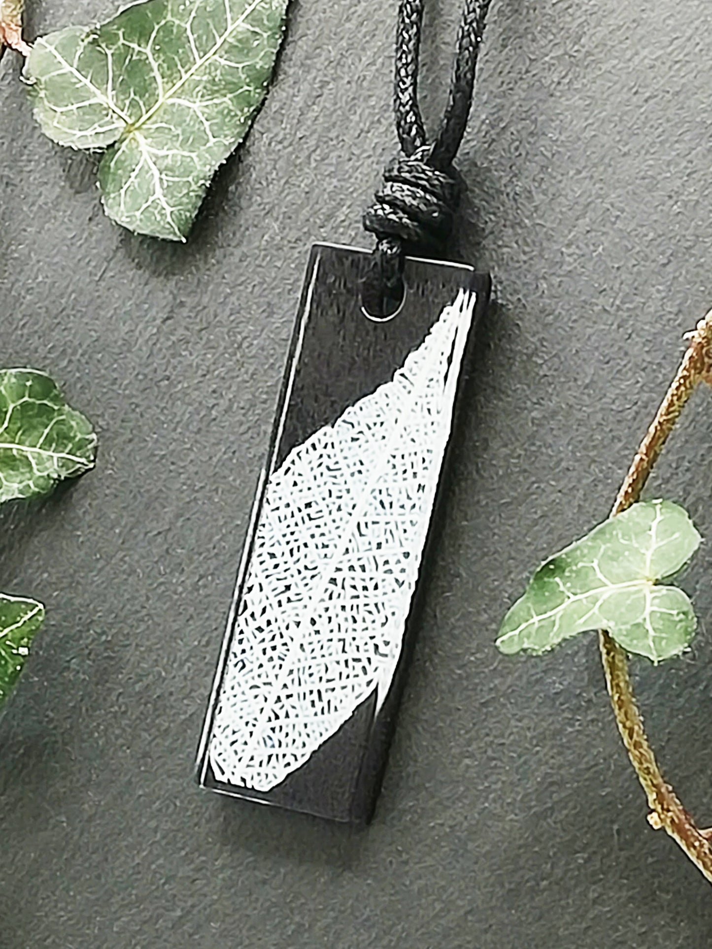 Black rectangular pendant with white leaf skeleton design, displayed at an angle to show the layers within the pendant