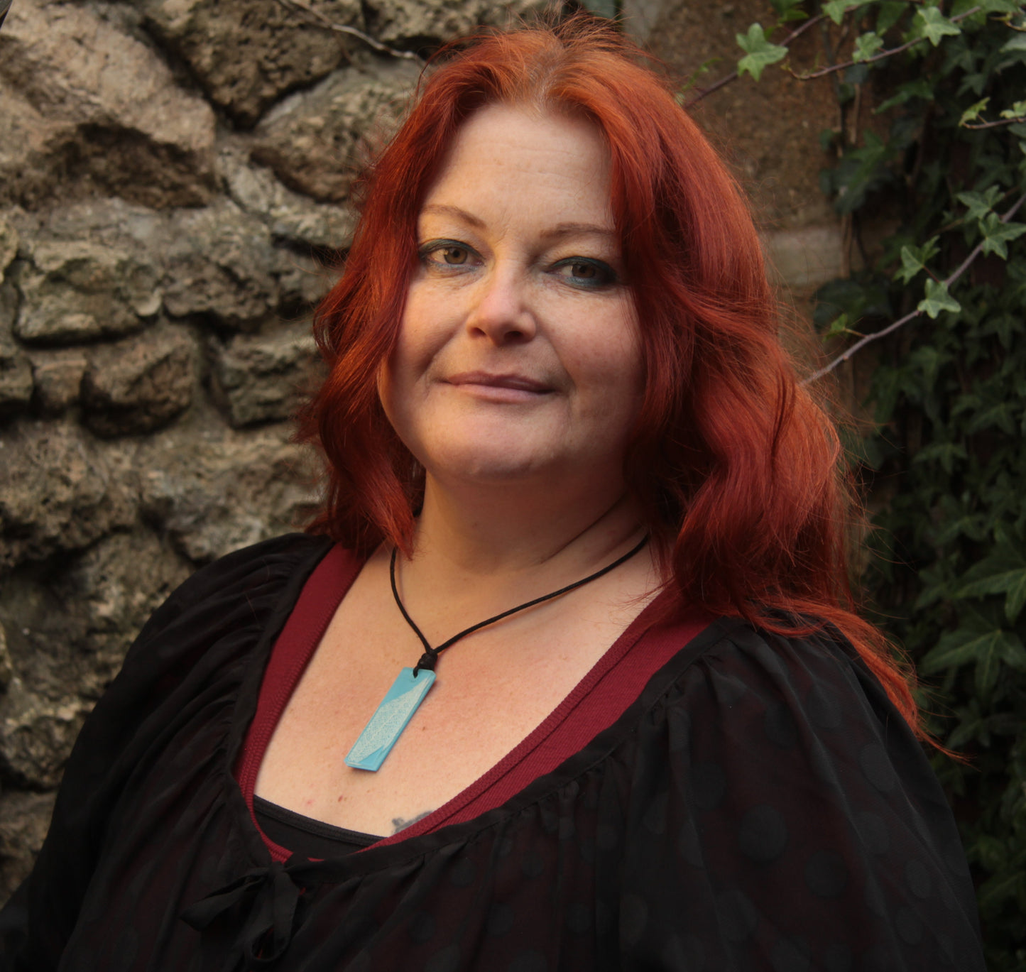 Red haired woman wearing a light blue rectangular pendant with white leaf skeleton design