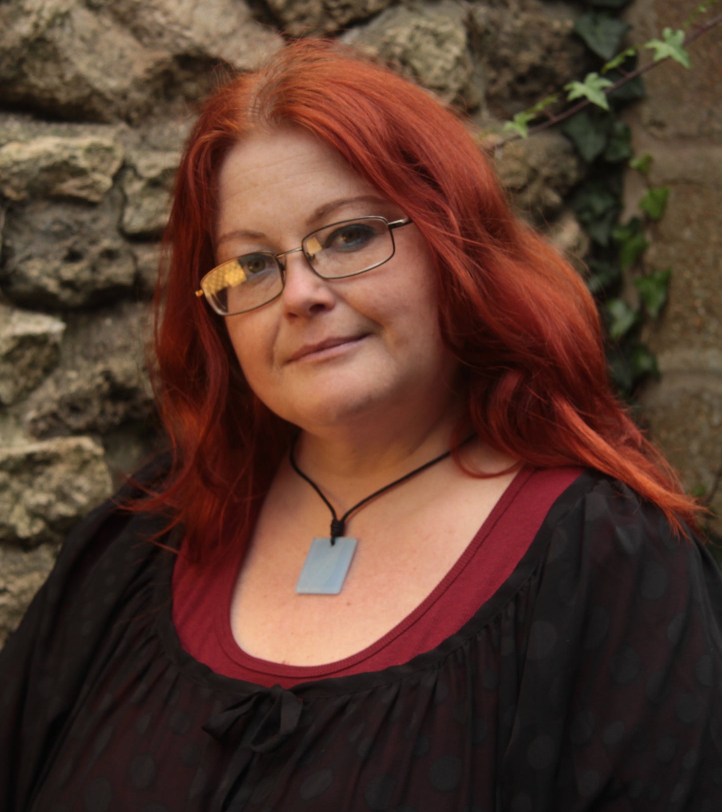 Red haired woman wearing a light blue rectangular pendant with white leaf skeleton design