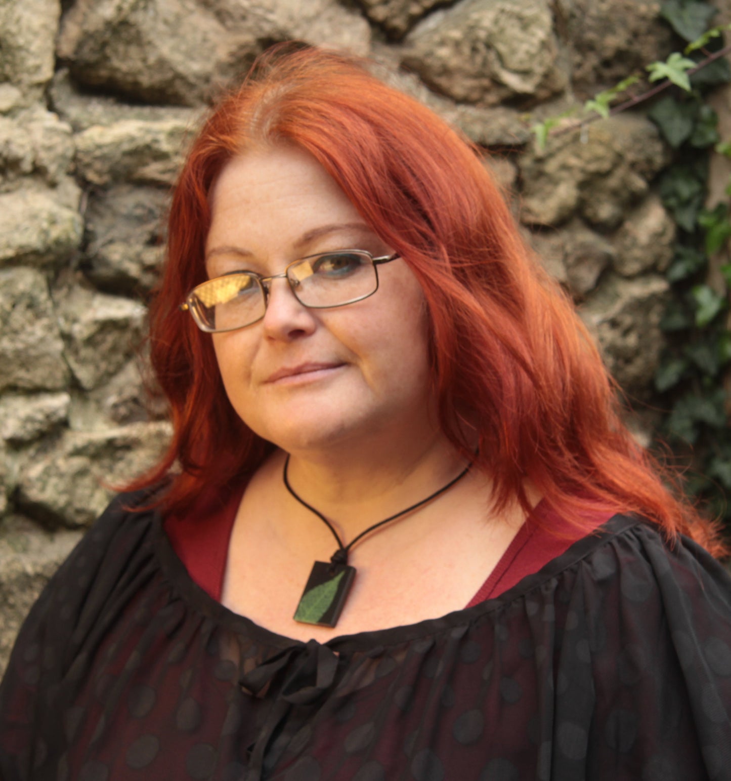 Red haired woman wearing a black rectangular pendant with bright green leaf skeleton design