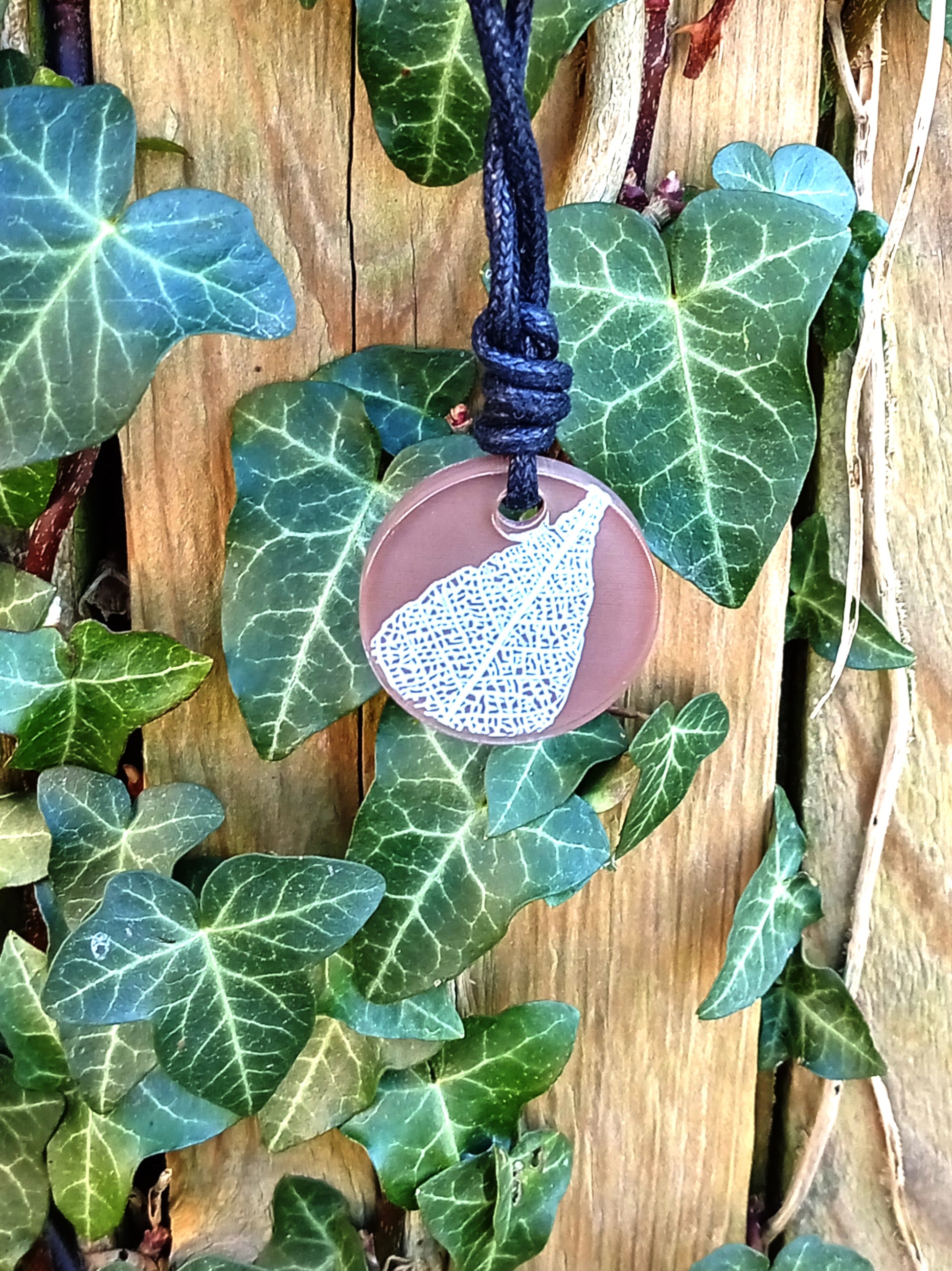 Warm brown round pendant with cream leaf skeleton design against ivy covered wood in natural daylight