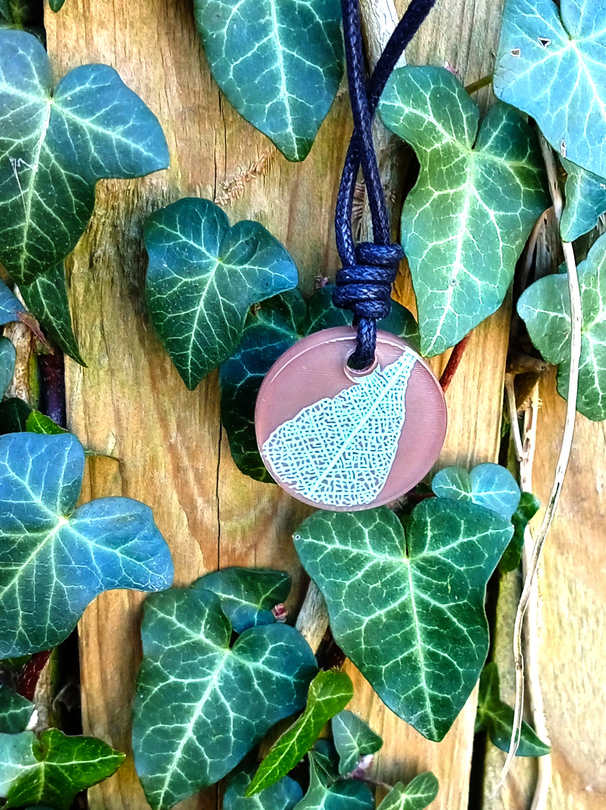 Warm brown round pendant with pale green leaf skeleton design against ivy covered wood in natural daylight