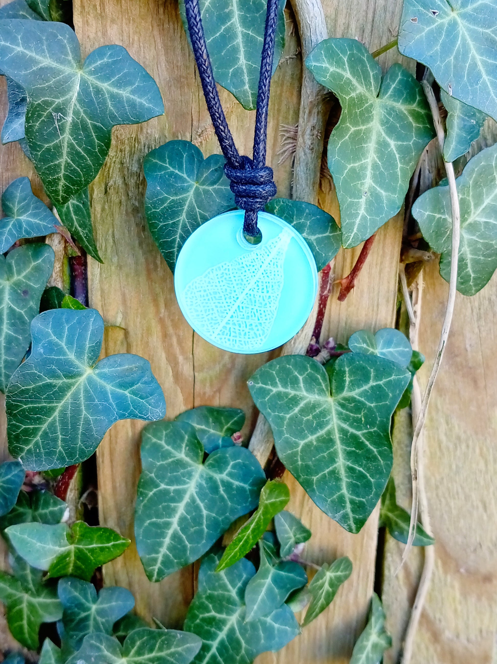 Light blue round pendant with white leaf skeleton design against ivy covered wood in natural daylight