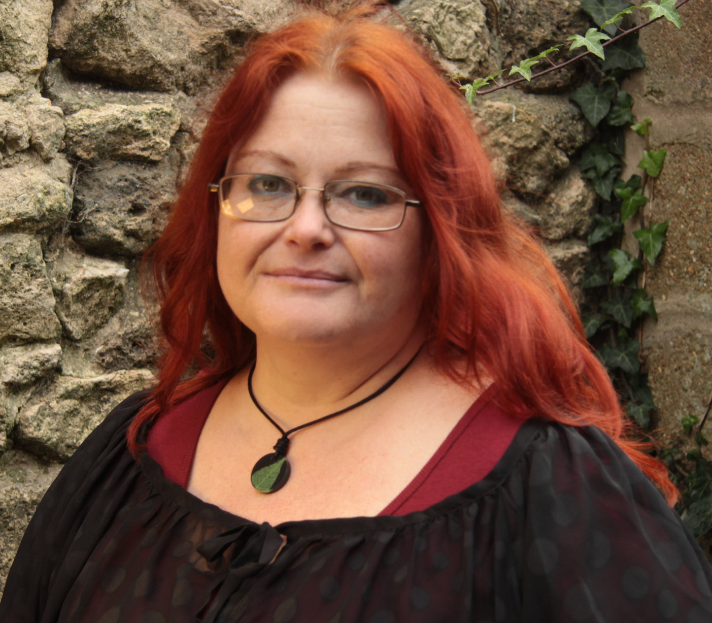Red haired woman wearing a black round pendant with bright green leaf skeleton design 