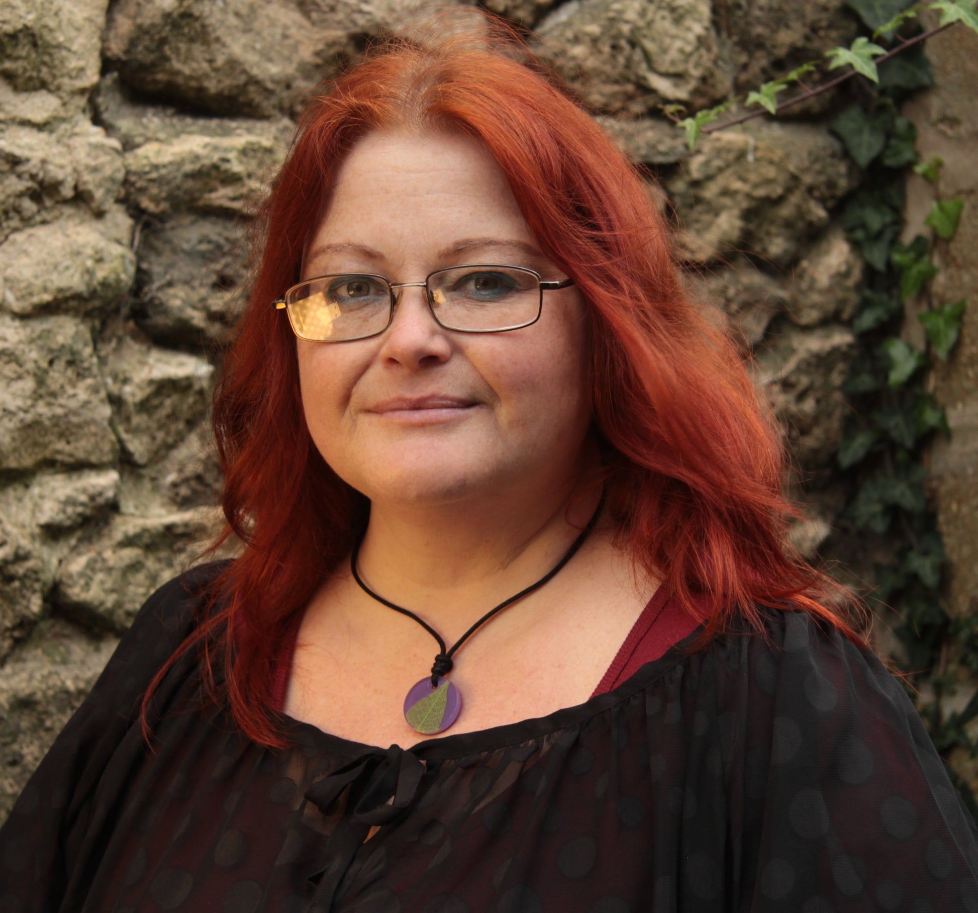 Red haired woman wearing a purple round pendant with bright green leaf skeleton design 