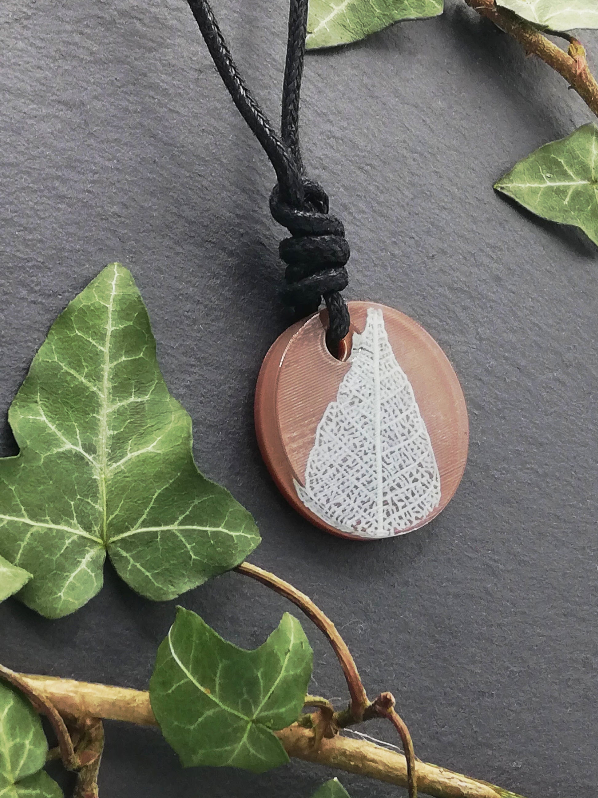 Warm brown round pendant with cream leaf skeleton design, displayed at an angle to show the layers within the pendant