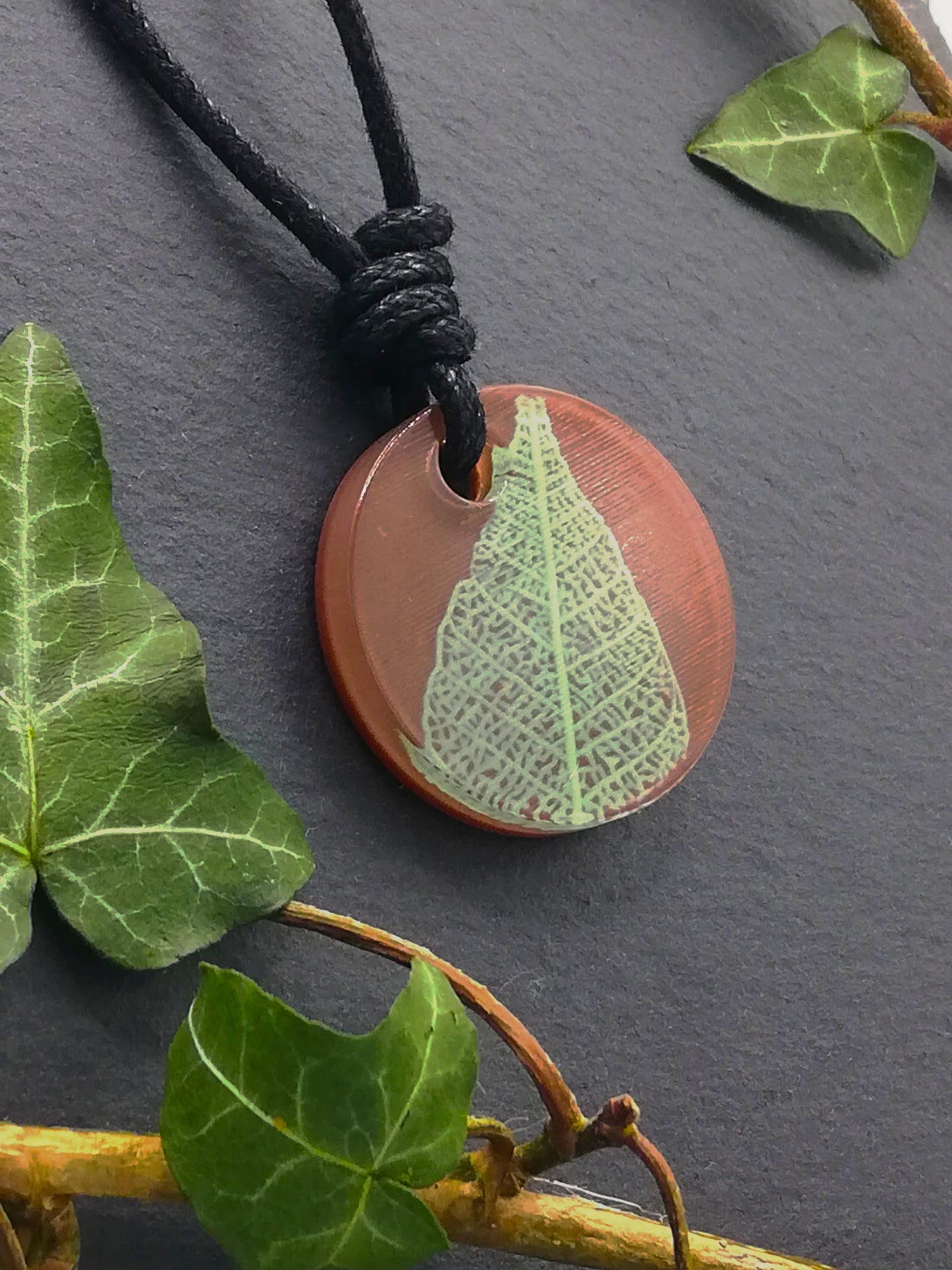 Warm brown round pendant with pale green leaf skeleton design, displayed at an angle to show the layers within the pendant