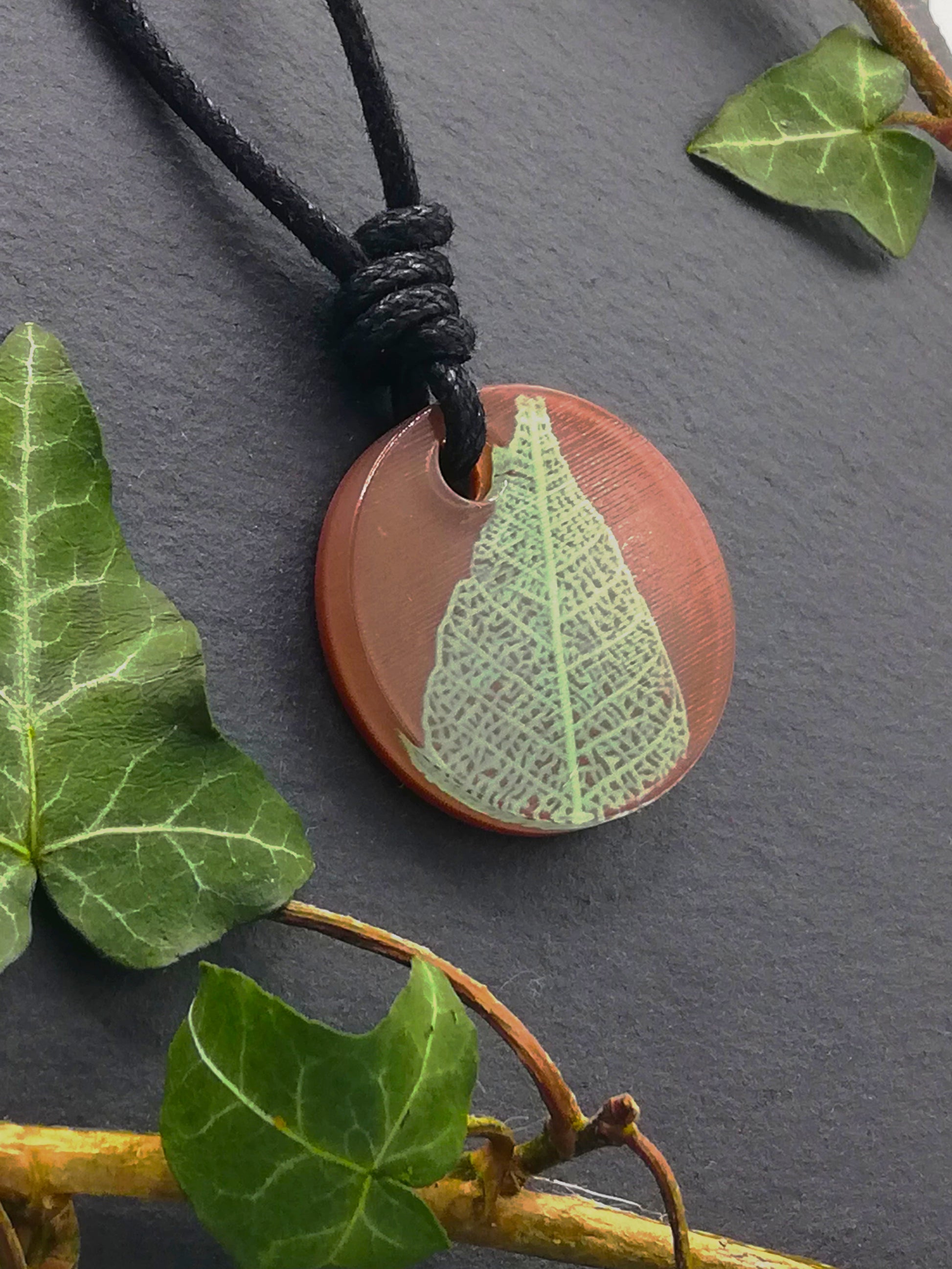 Warm brown round pendant with pale green leaf skeleton design, displayed at an angle to show the layers within the pendant