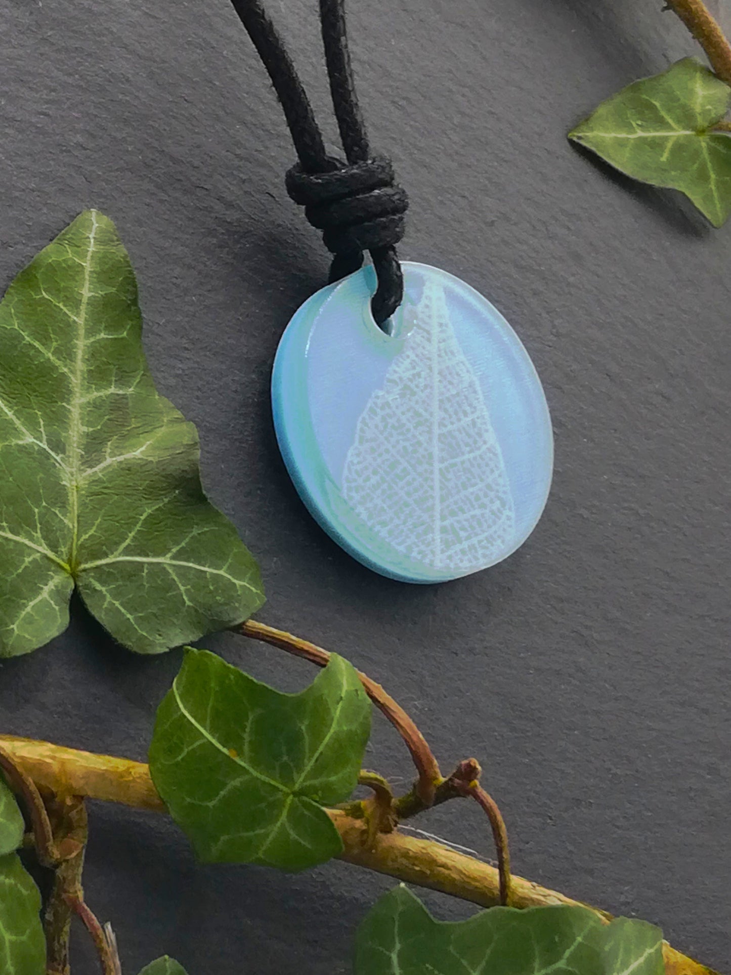Light blue round pendant with white leaf skeleton design, displayed at an angle to show the layers within the pendant
