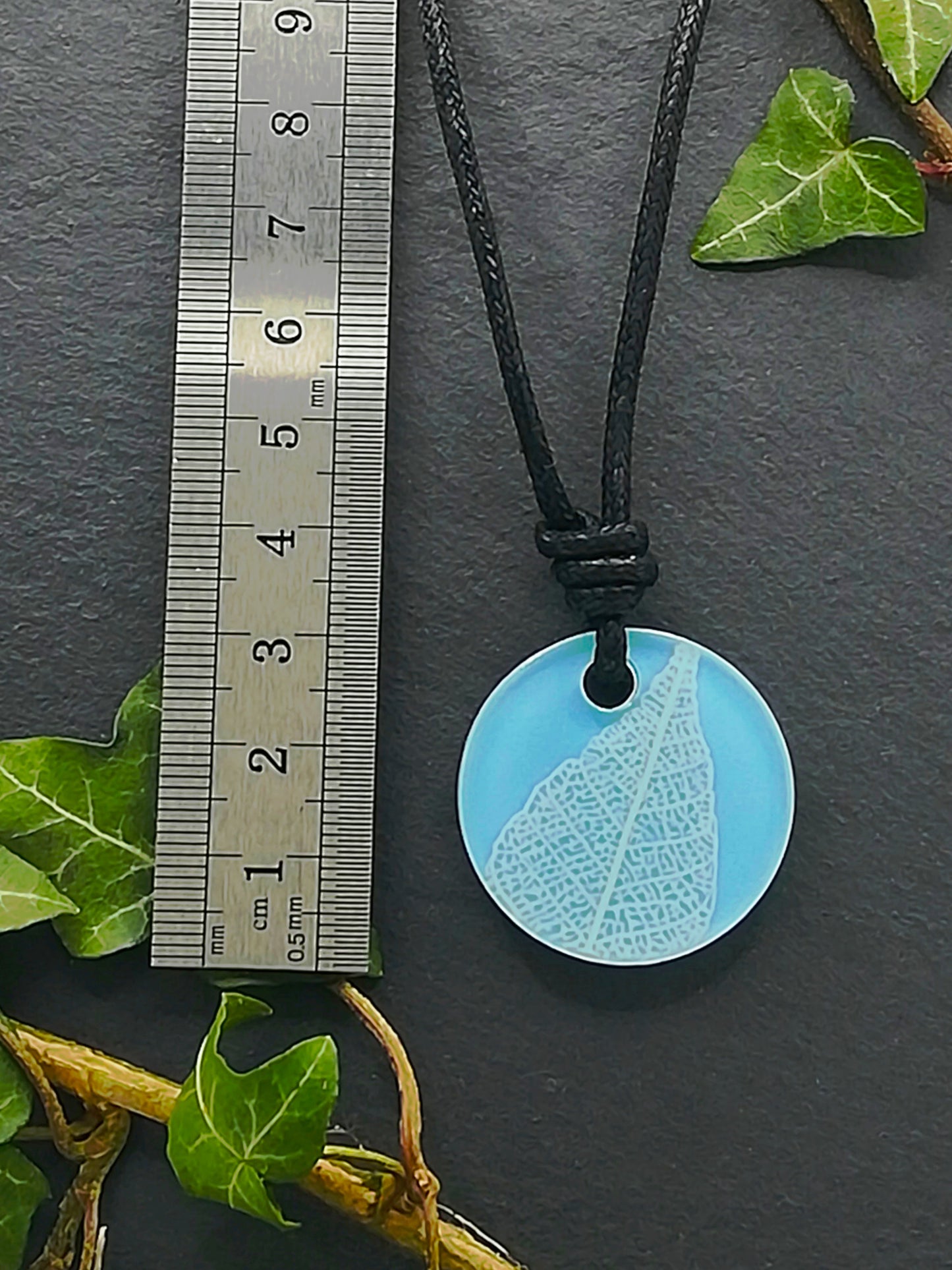 Light blue round pendant with white leaf skeleton design shown next to a ruler displaying centimetres for scale