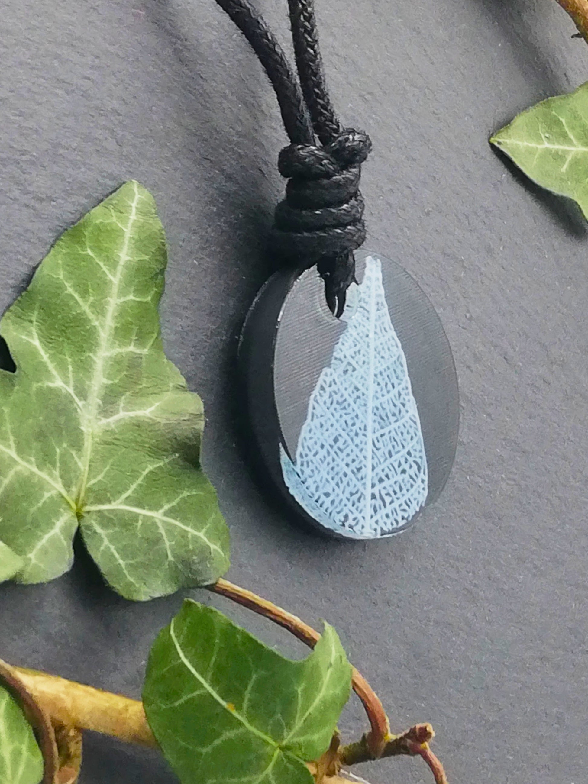 Black round pendant with white leaf skeleton design, displayed at an angle to show the layers within the pendant