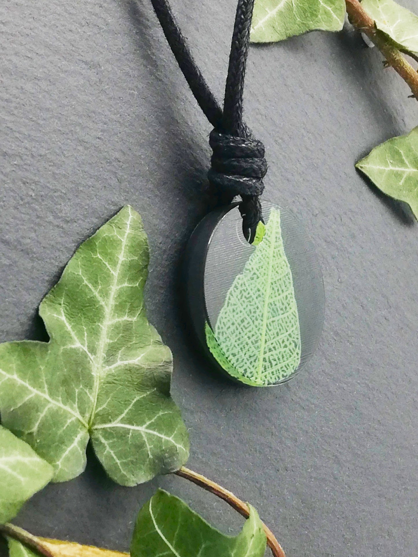 Black round pendant with bright green leaf skeleton design, displayed at an angle to show the layers within the pendant