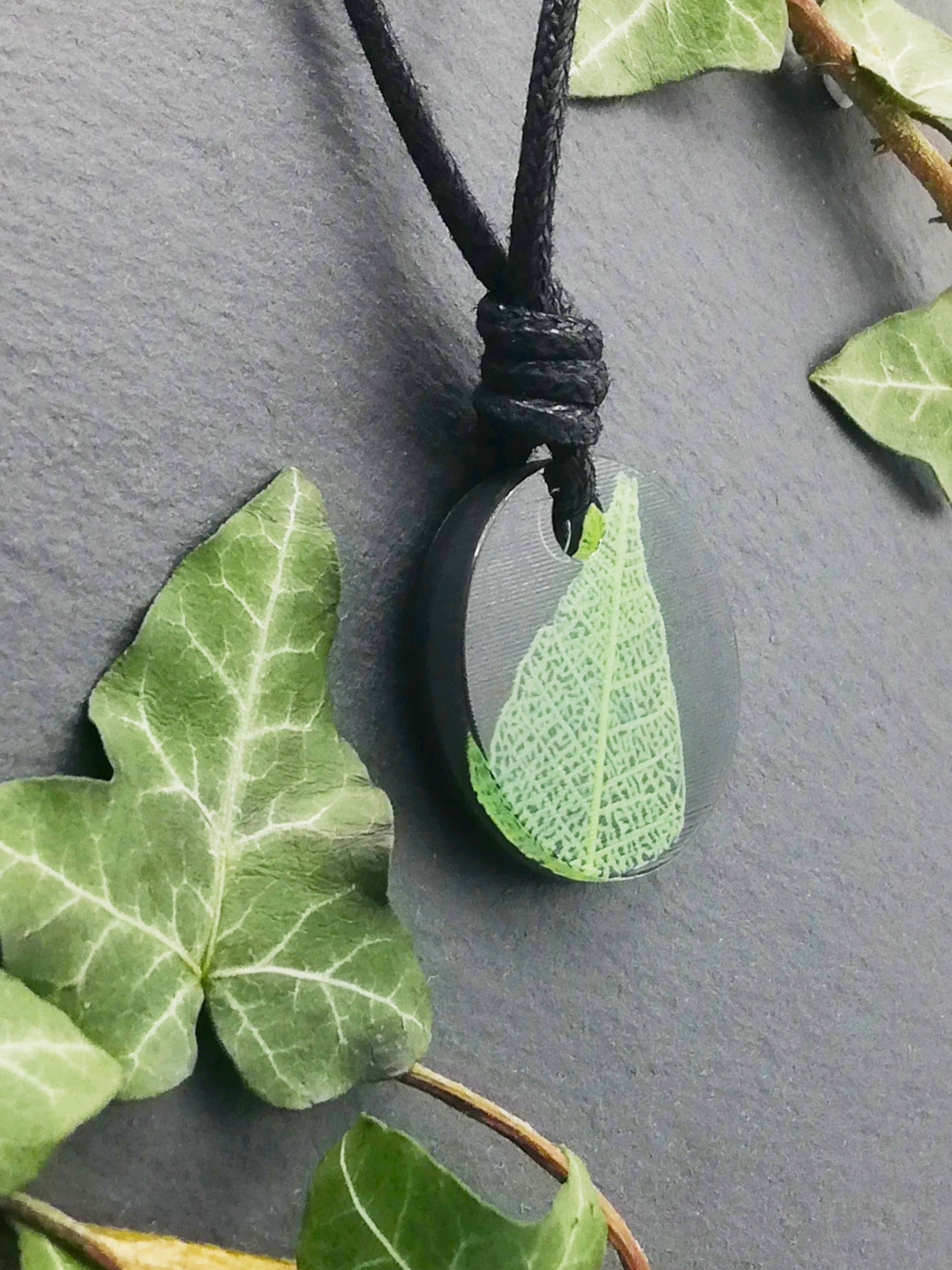 Black round pendant with bright green leaf skeleton design, displayed at an angle to show the layers within the pendant