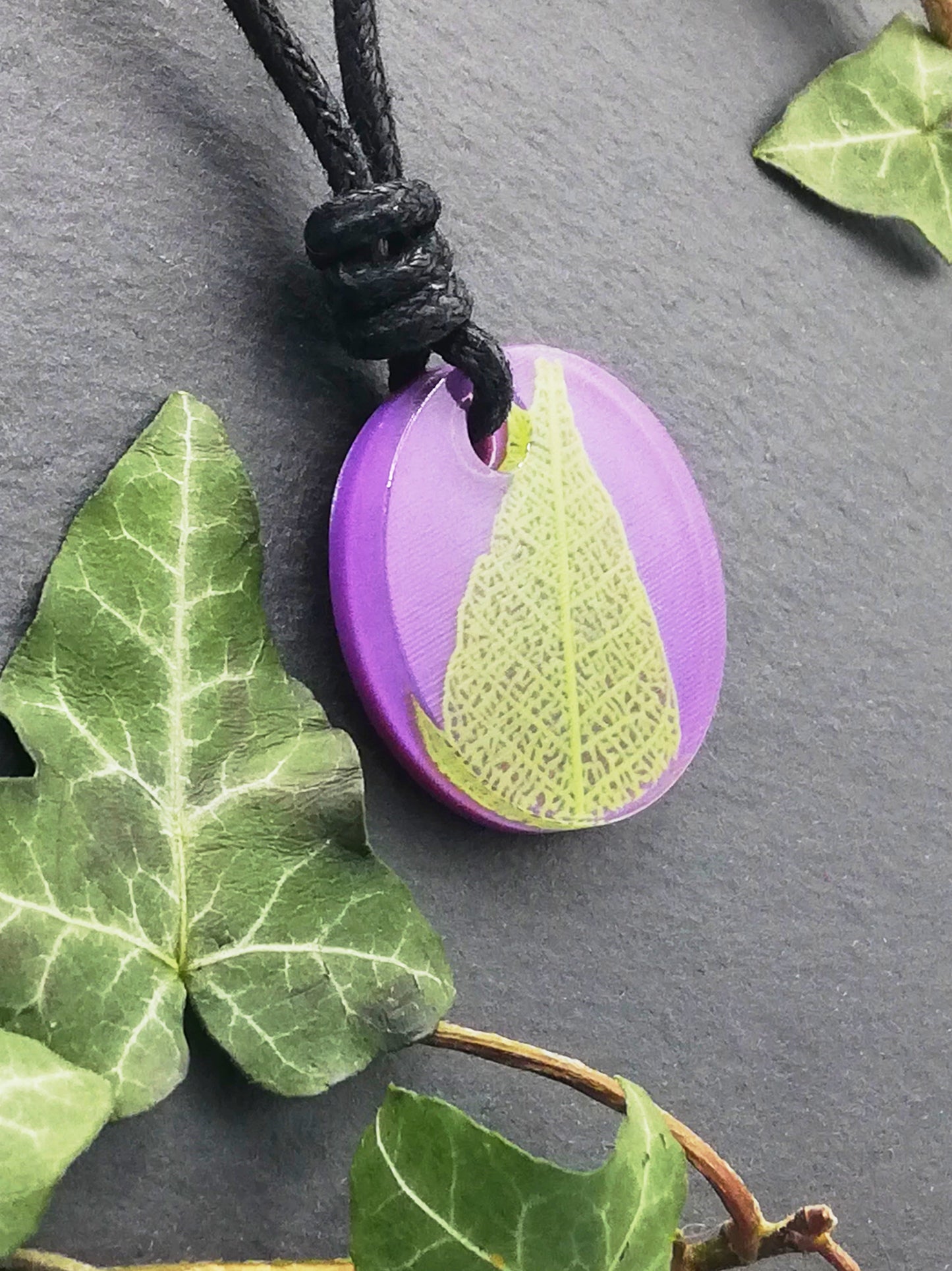 Purple round pendant with bright green leaf skeleton design, displayed at an angle to show the layers within the pendant