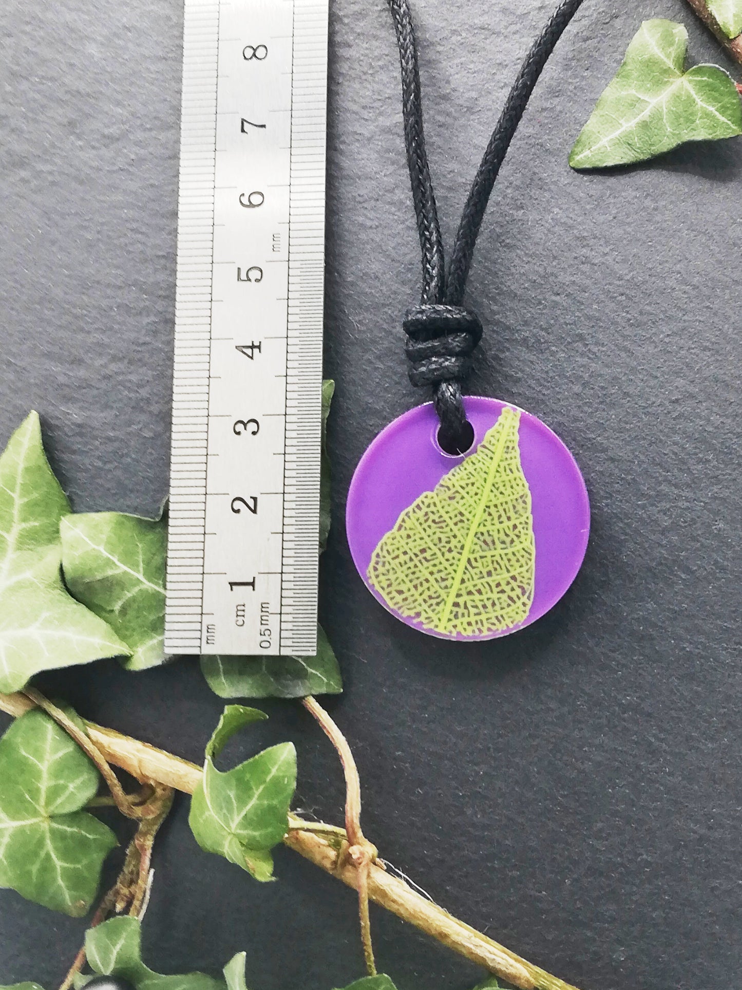 Purple round pendant with bright green leaf skeleton design shown next to a ruler displaying centimetres for scale