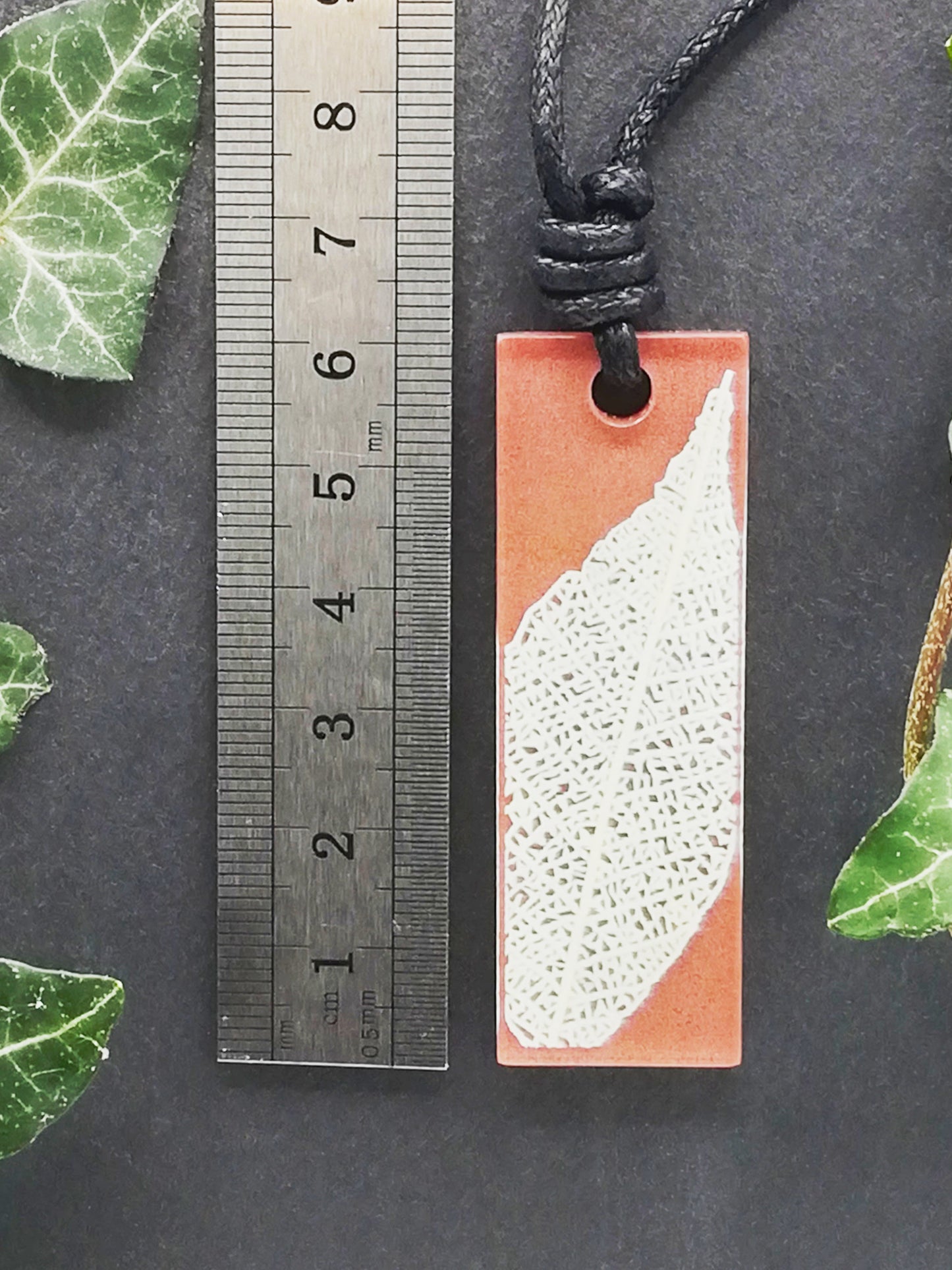 Warm brown rectangular pendant with cream leaf skeleton design shown next to a ruler displaying centimetres for scale