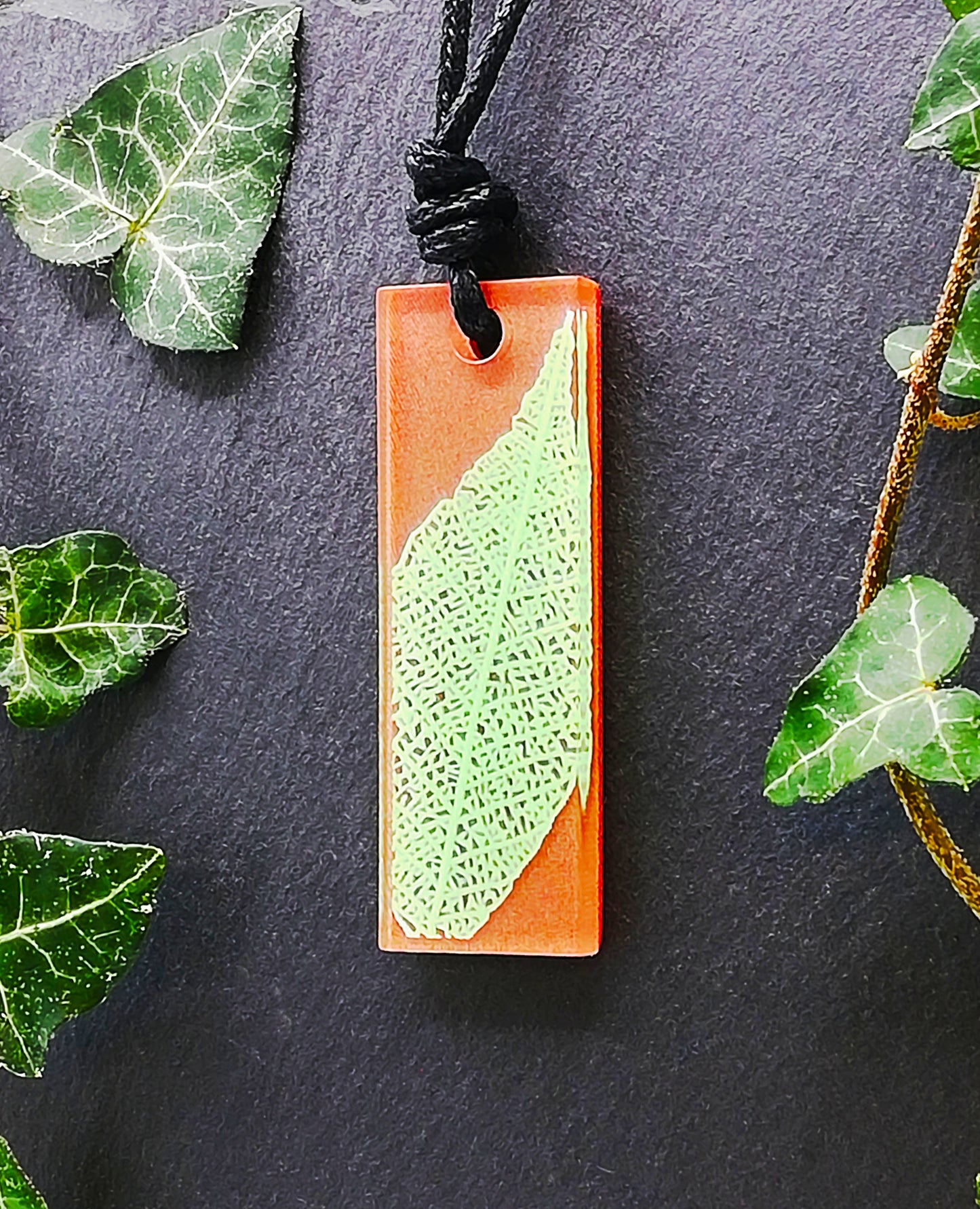 Warm brown rectangular pendant with pale green leaf skeleton design, displayed at an angle to show the layers within the pendant
