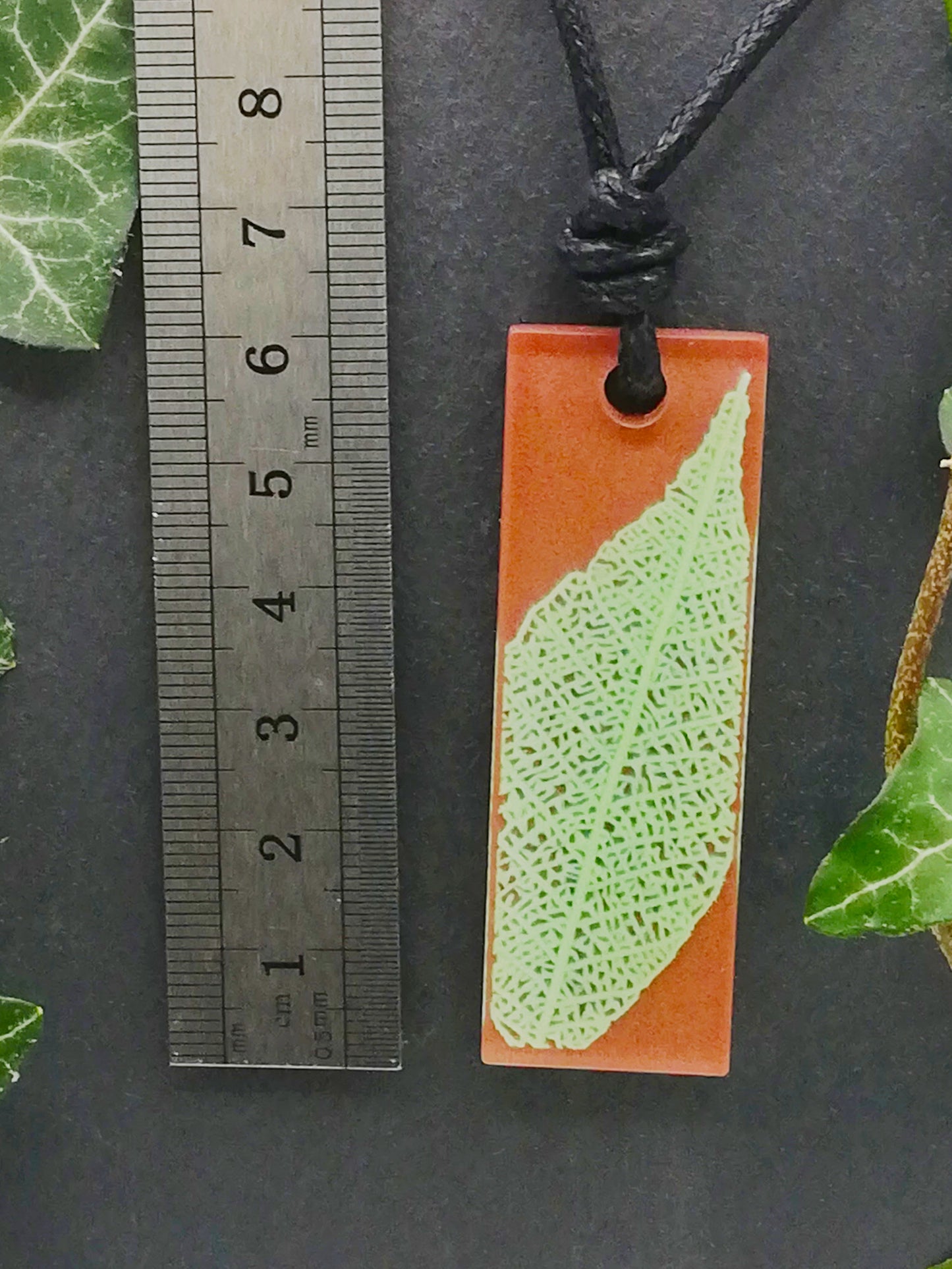 Warm brown rectangular pendant with pale green leaf skeleton design shown next to a ruler displaying centimetres for scale