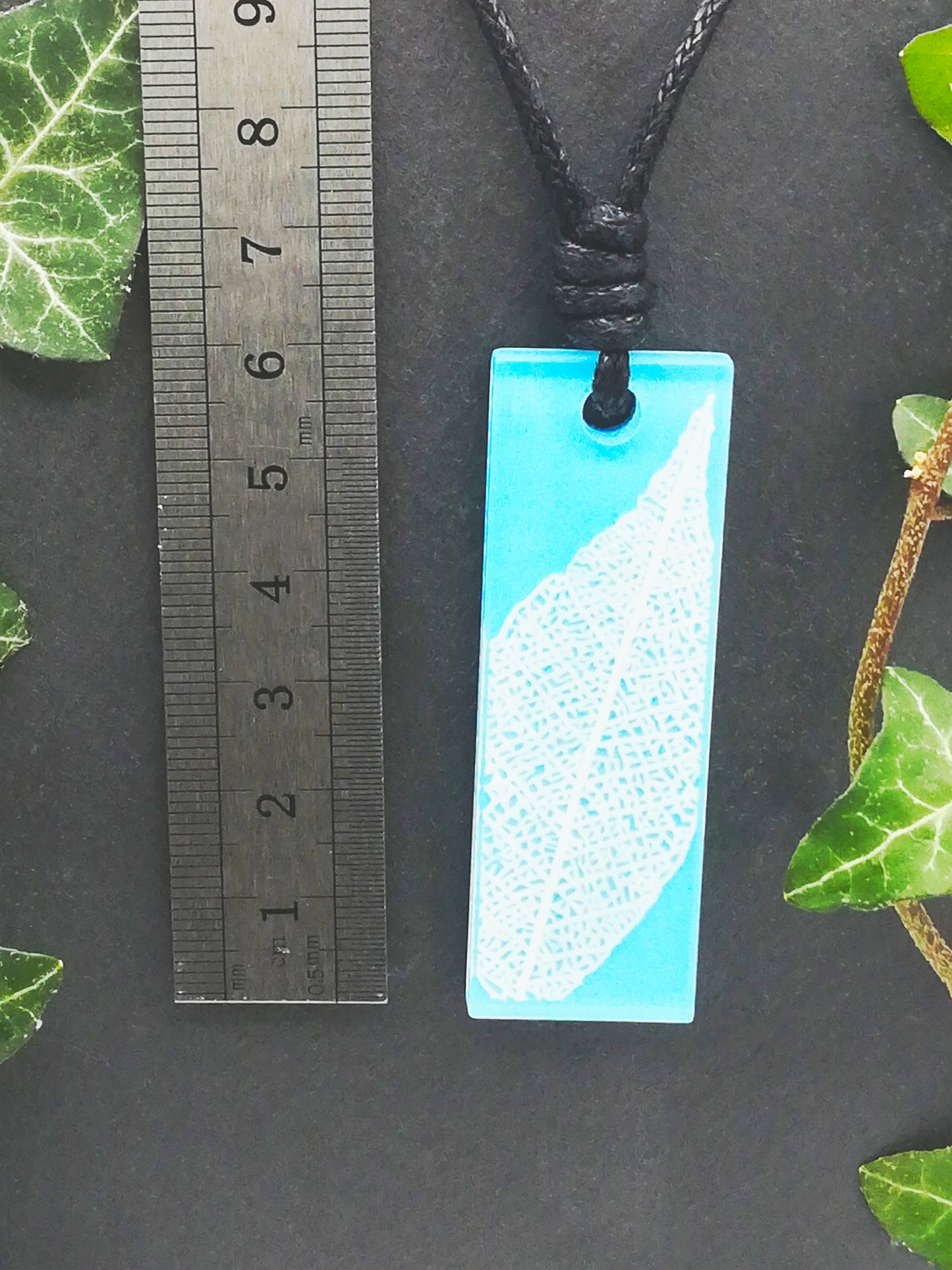 Light blue rectangular pendant with white leaf skeleton design shown next to a ruler displaying centimetres for scale