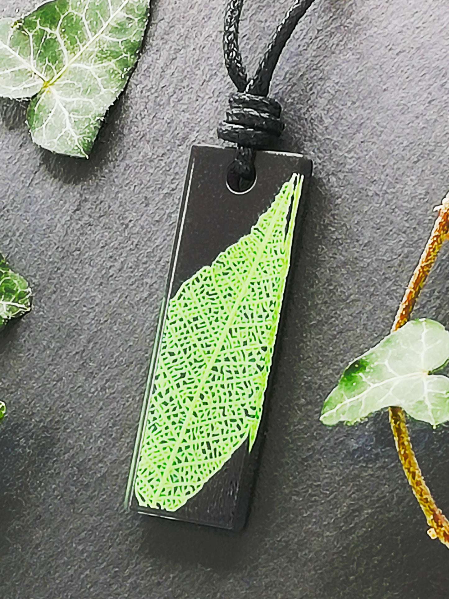 Black rectangular pendant with bright green leaf skeleton design, displayed at an angle to show the layers within the pendant