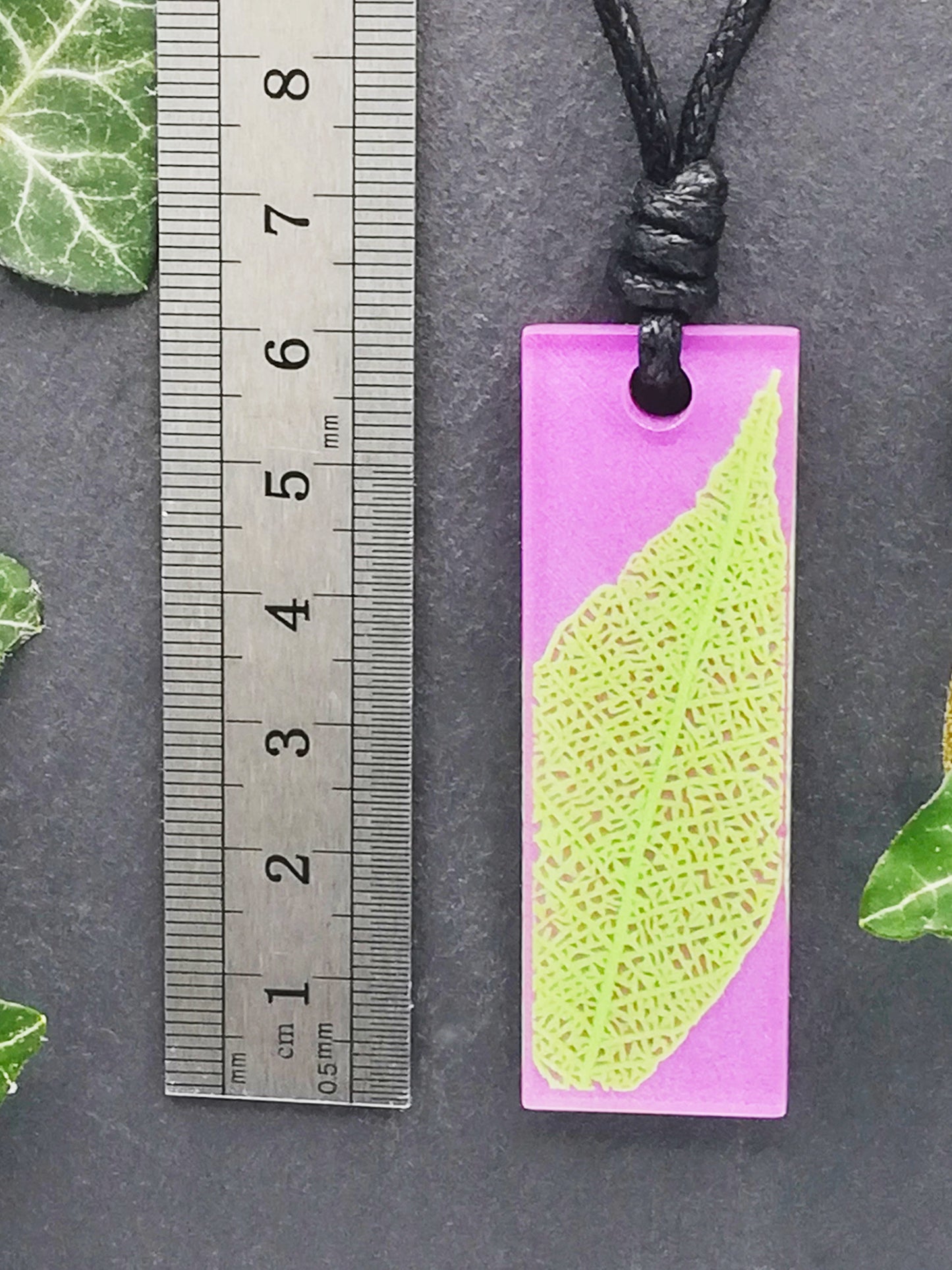 Purple rectangular pendant with bright green leaf skeleton design shown next to a ruler displaying centimetres for scale