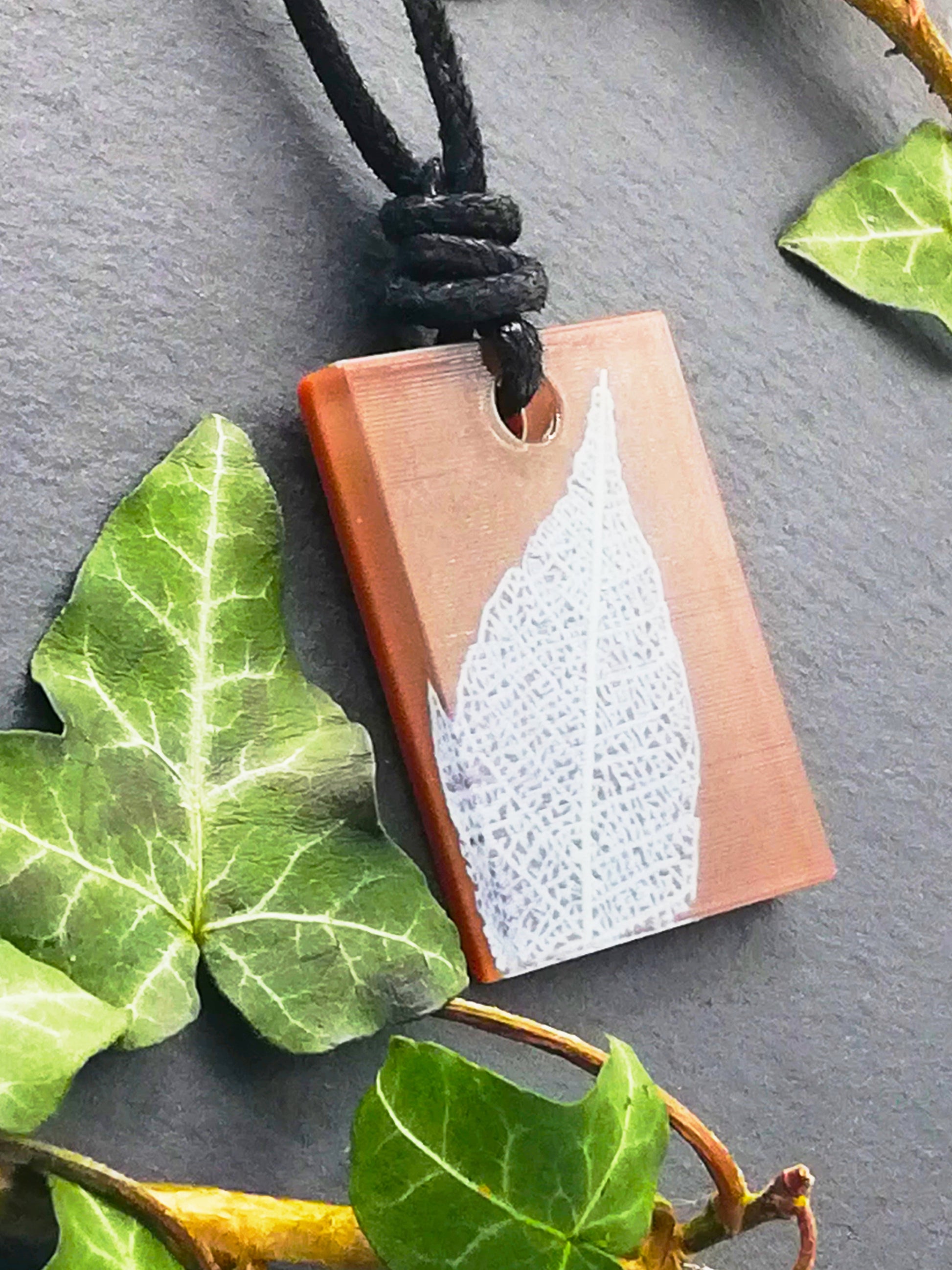 Warm brown rectangular pendant with cream leaf skeleton design, displayed at an angle to show the layers within the pendant