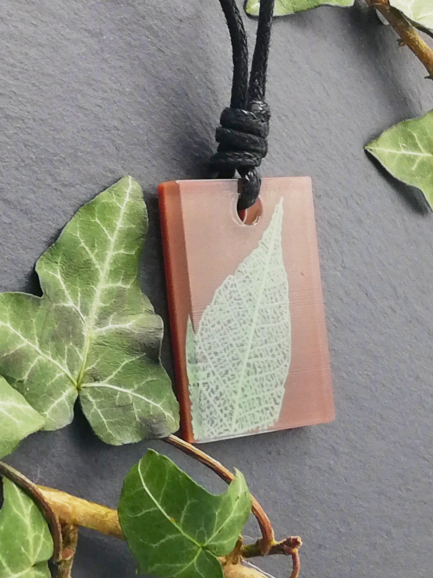 Warm brown rectangular pendant with pale green leaf skeleton design, displayed at an angle to show the layers within the pendant