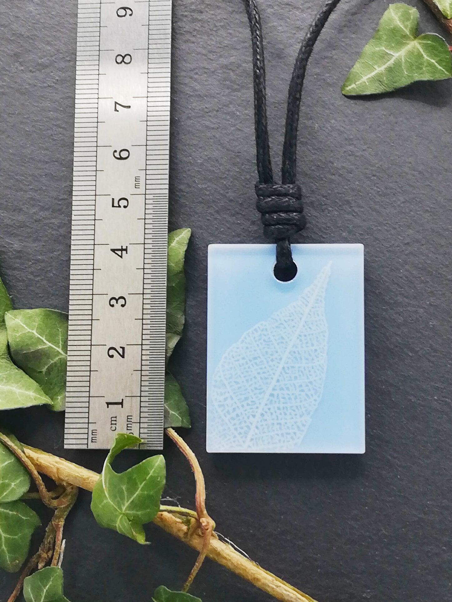 Light blue rectangular pendant with white leaf skeleton design shown next to a ruler displaying centimetres for scale