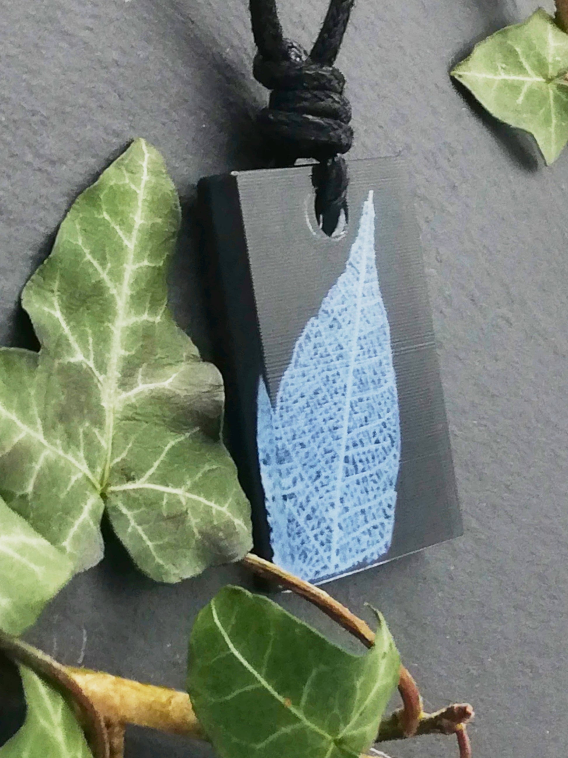 Black rectangular pendant with white leaf skeleton design, displayed at an angle to show the layers within the pendant