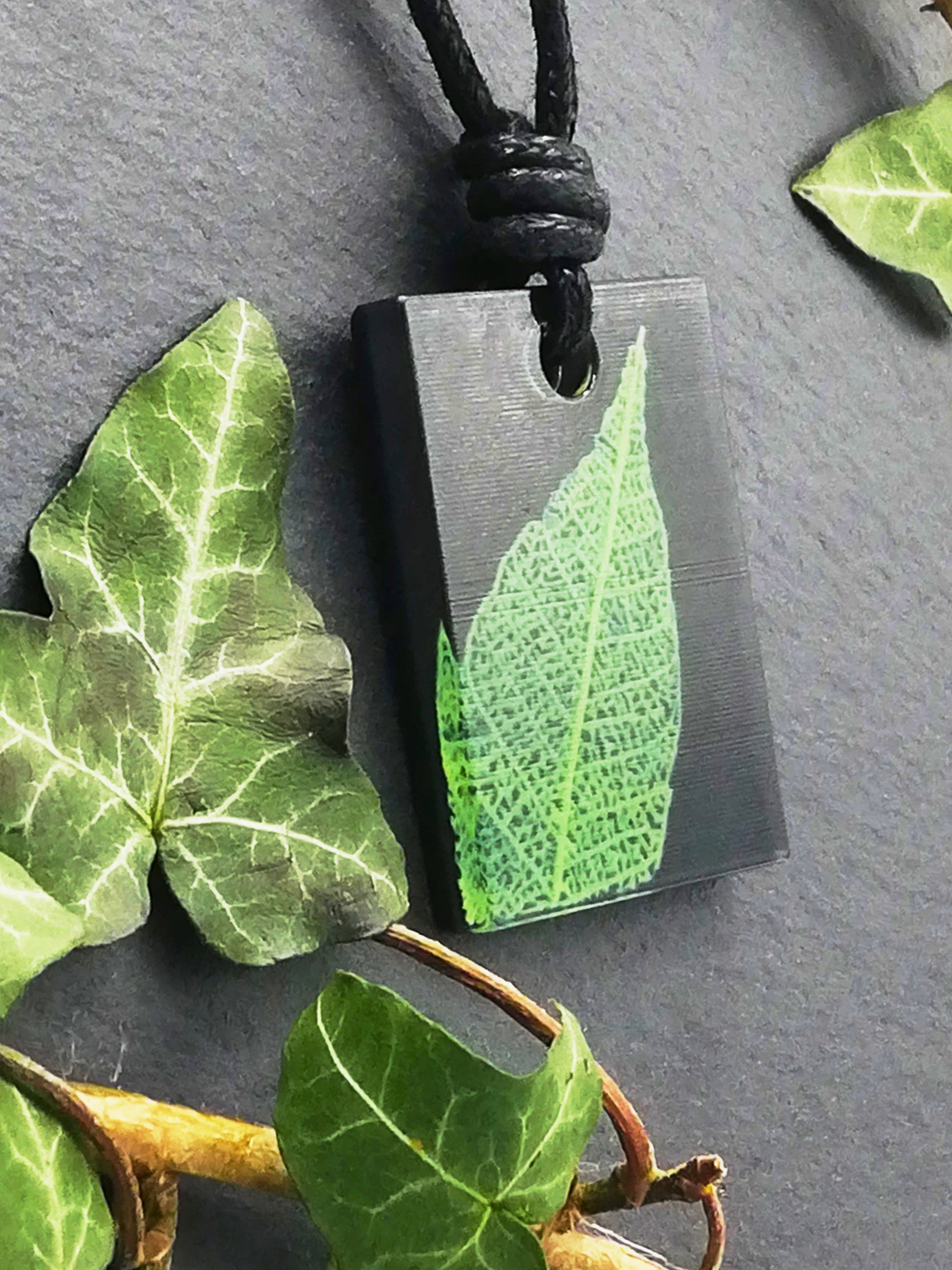 Black rectangular pendant with bright green leaf skeleton design, displayed at an angle to show the layers within the pendant