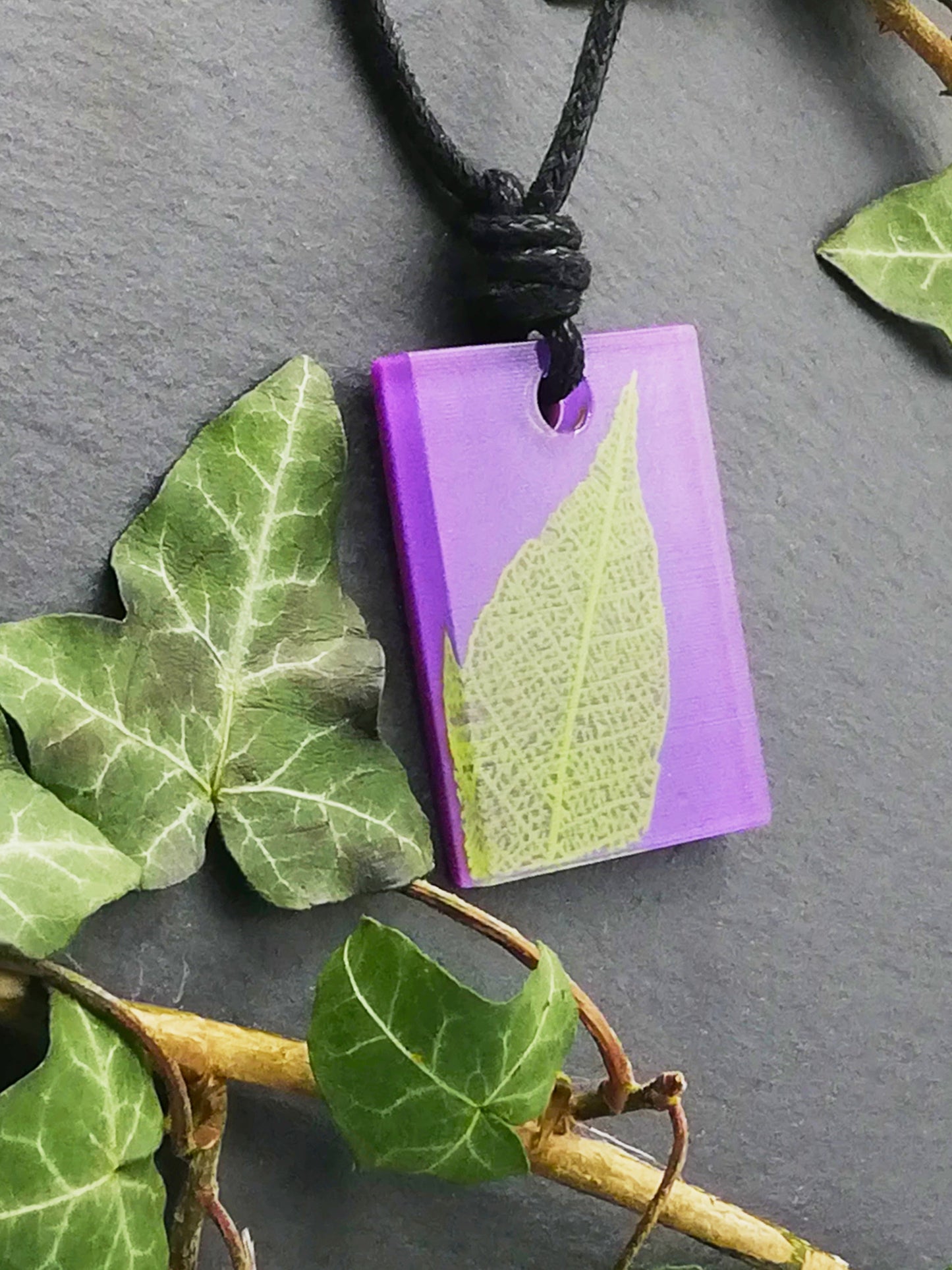 Purple rectangular pendant with bright green leaf skeleton design, displayed at an angle to show the layers within the pendant