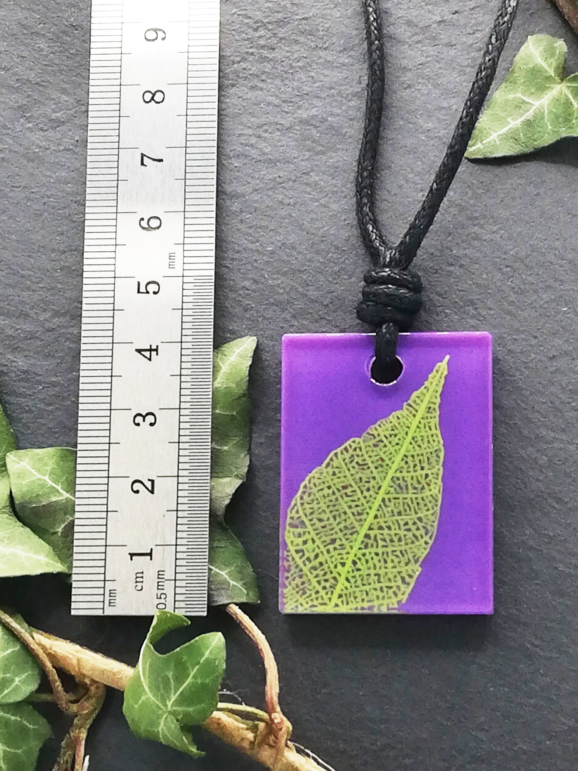 Purple rectangular pendant with bright green leaf skeleton design shown next to a ruler displaying centimetres for scale
