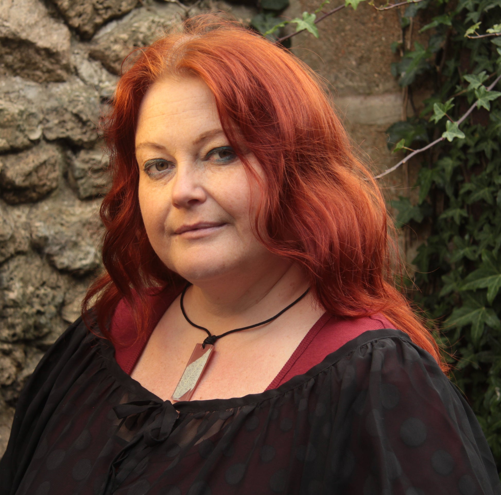 Red haired woman wearing a warm brown rectangular pendant with cream leaf skeleton design 