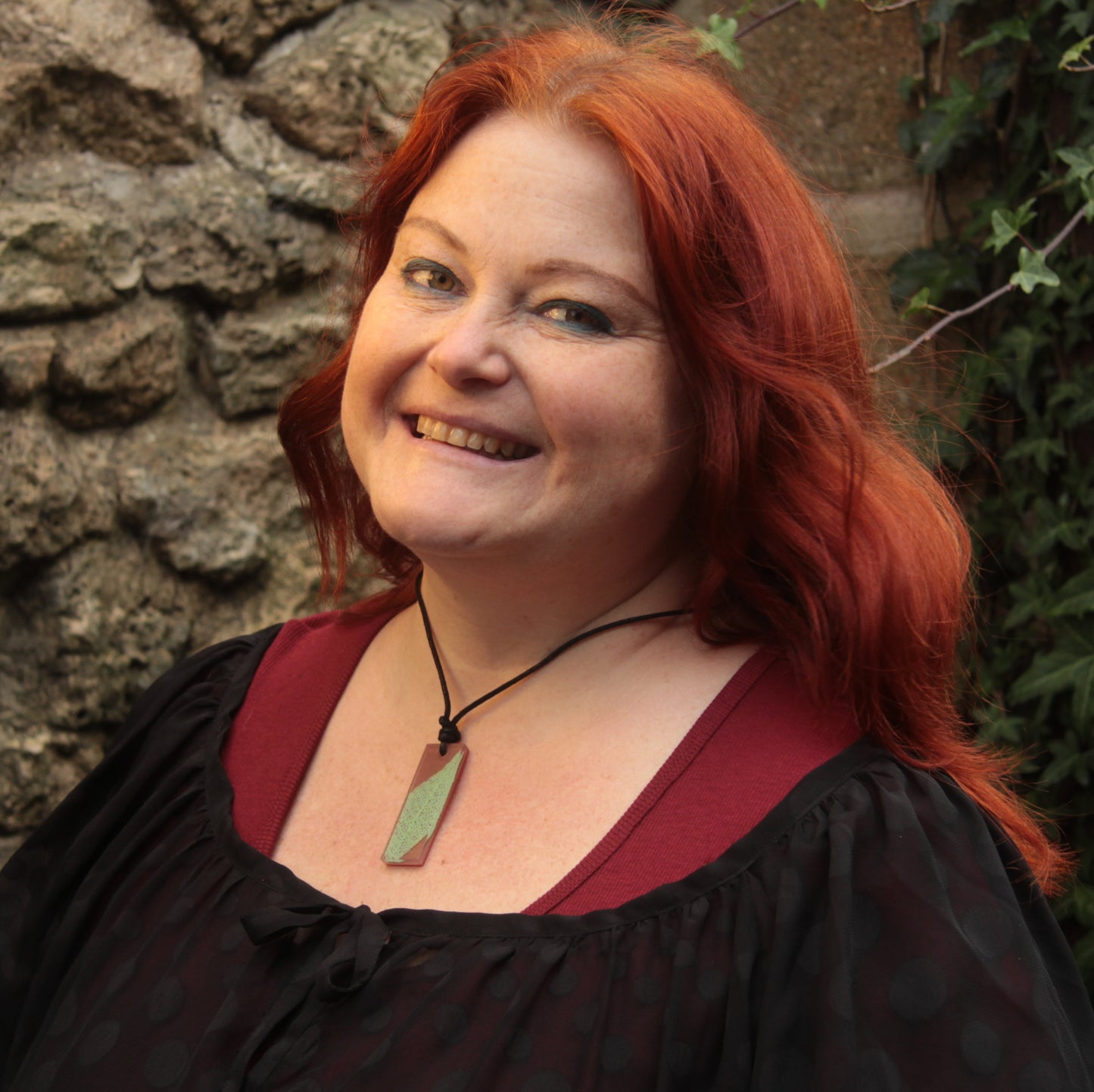 Red haired woman wearing a warm brown rectangular pendant with pale green leaf skeleton design 
