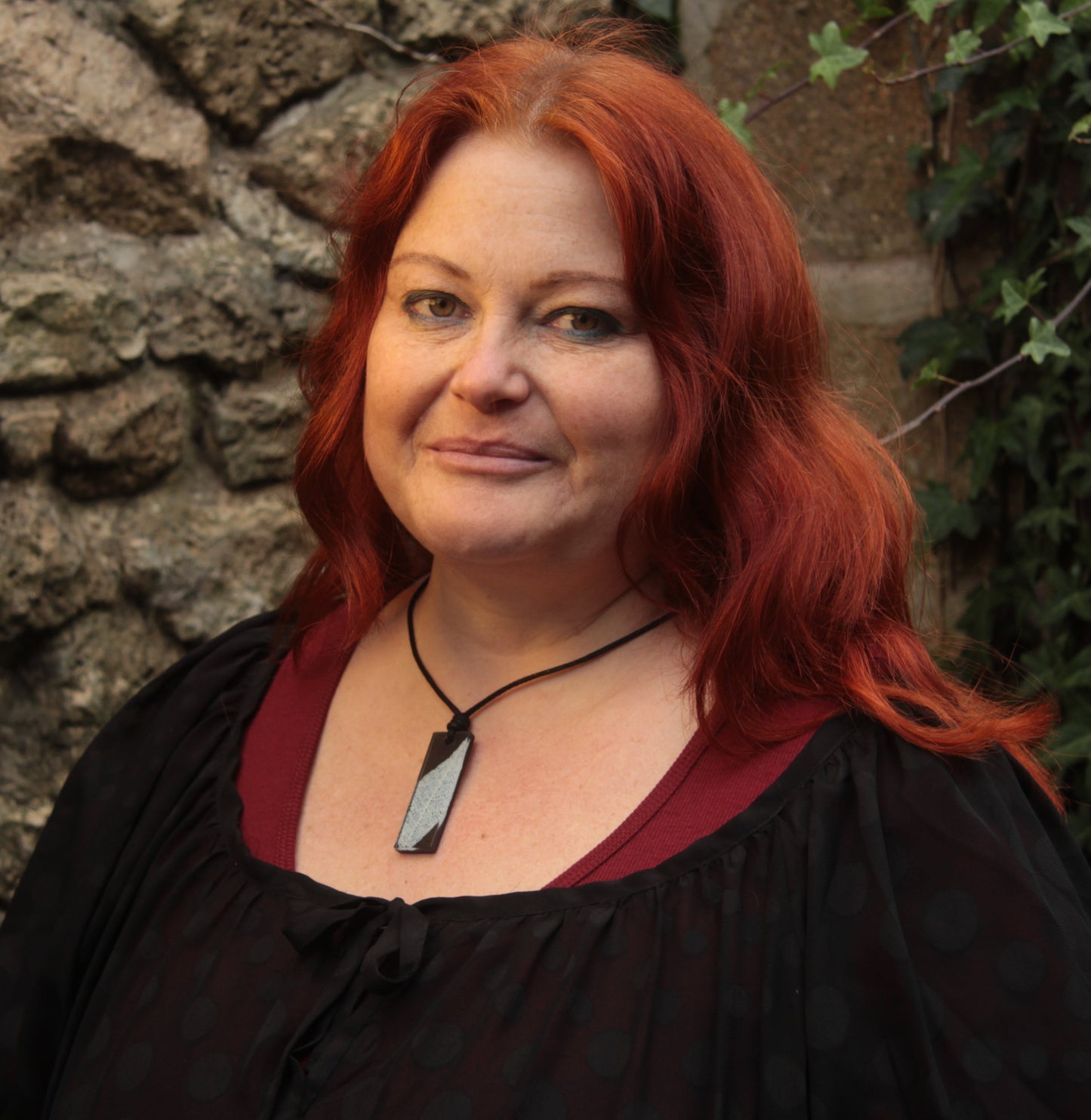 Red haired woman wearing a black rectangular pendant with white leaf skeleton design 