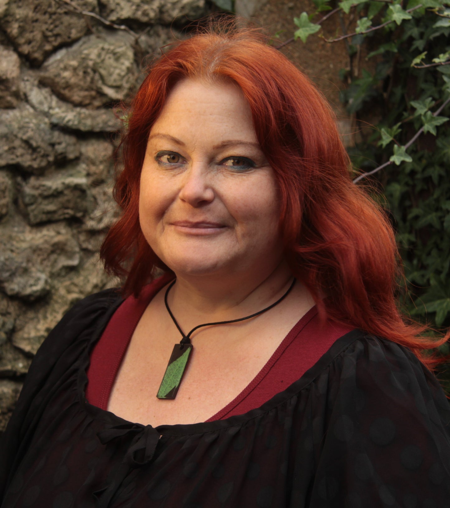 Red haired woman wearing a black rectangular pendant with bright green leaf skeleton design 