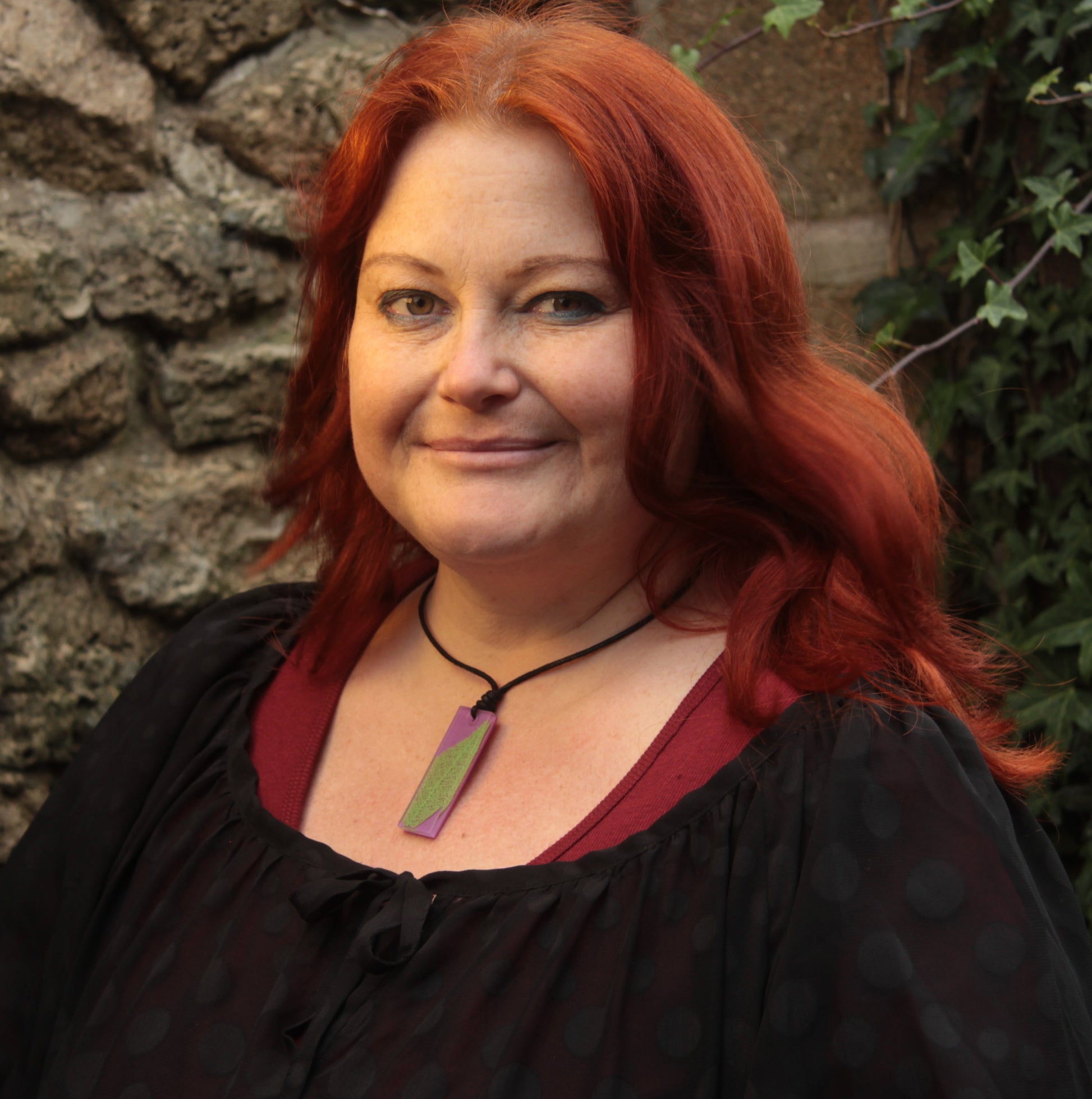Red haired woman wearing a purple rectangular pendant with bright green leaf skeleton design 