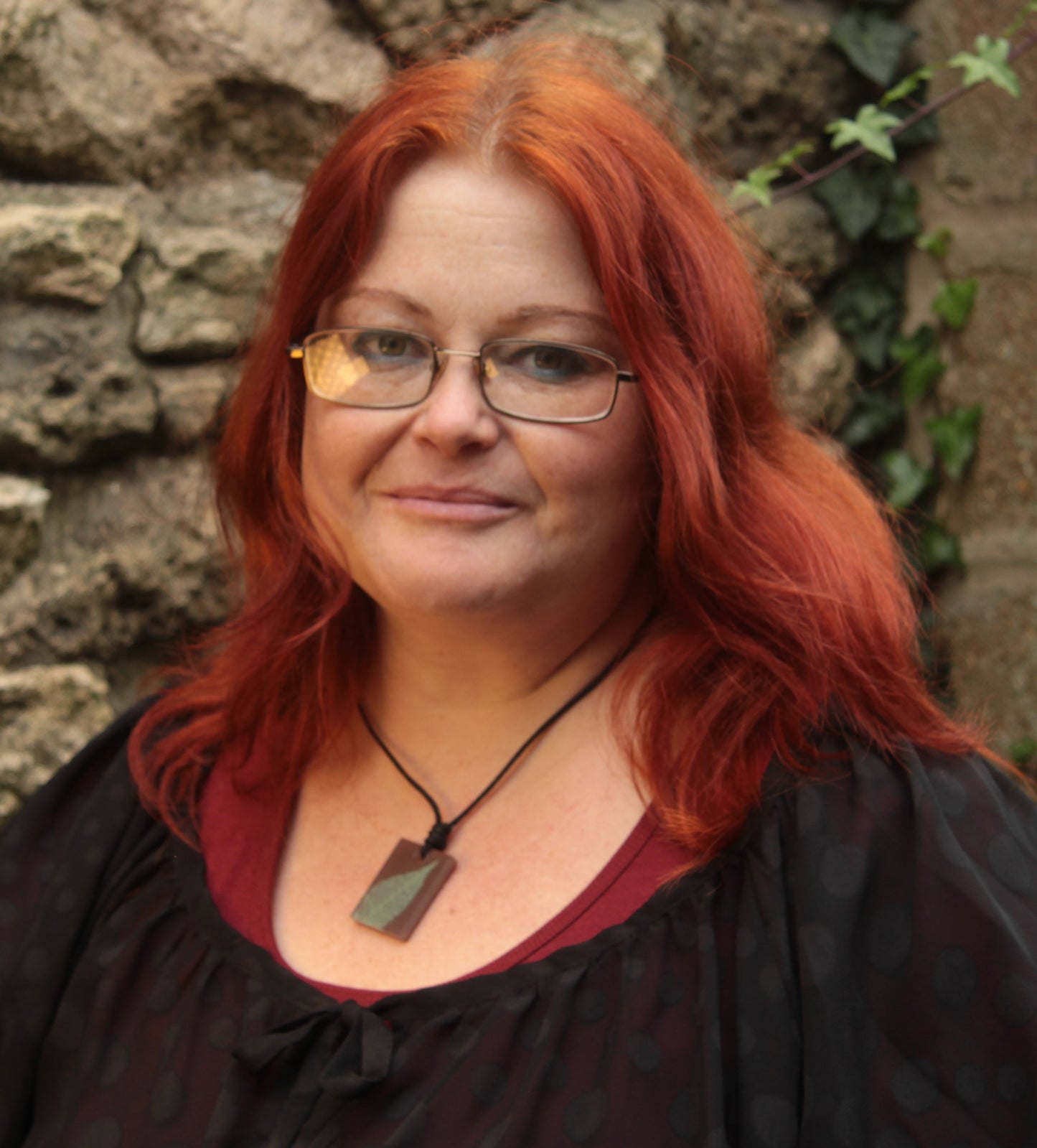 Red haired woman wearing a warm brown rectangular pendant with pale green leaf skeleton design 
