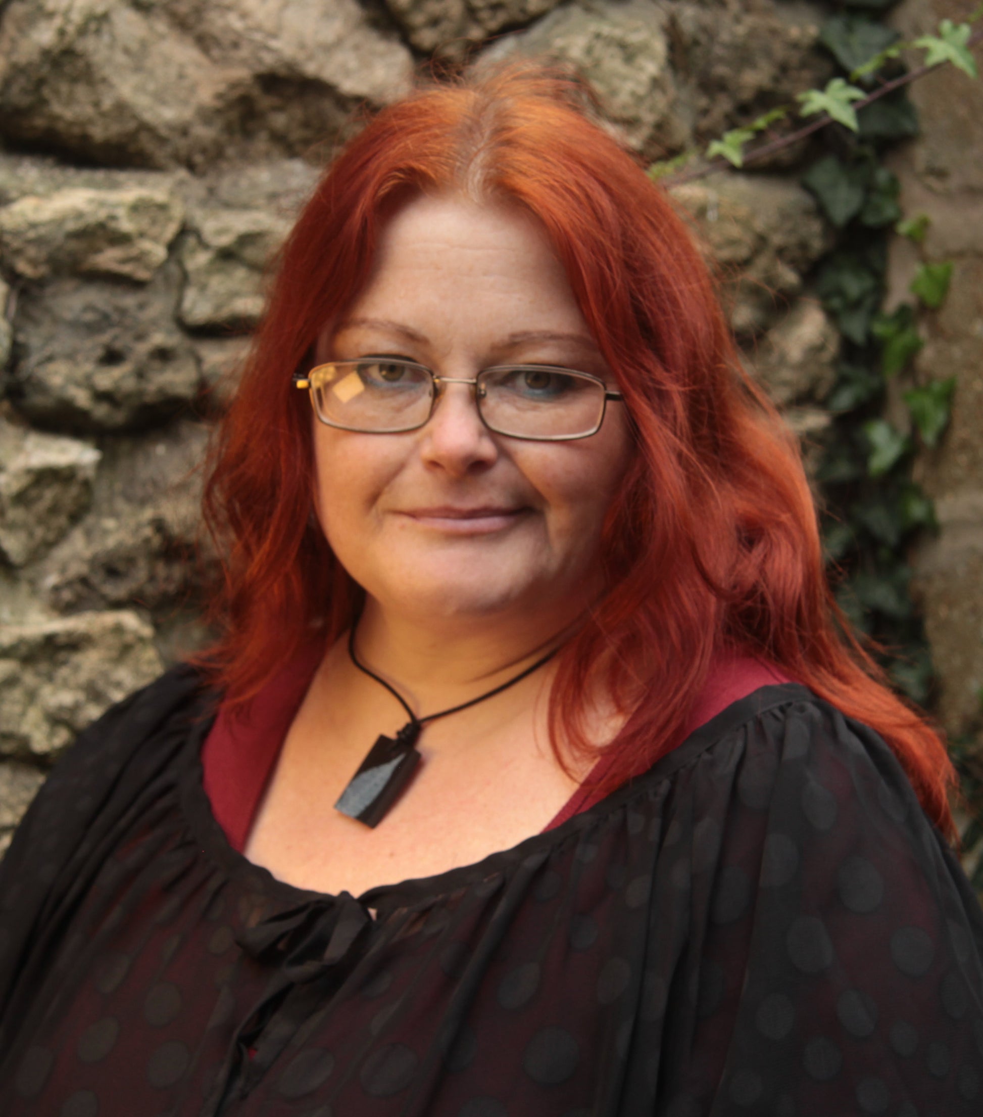 Red haired woman wearing a black rectangular pendant with white leaf skeleton design 